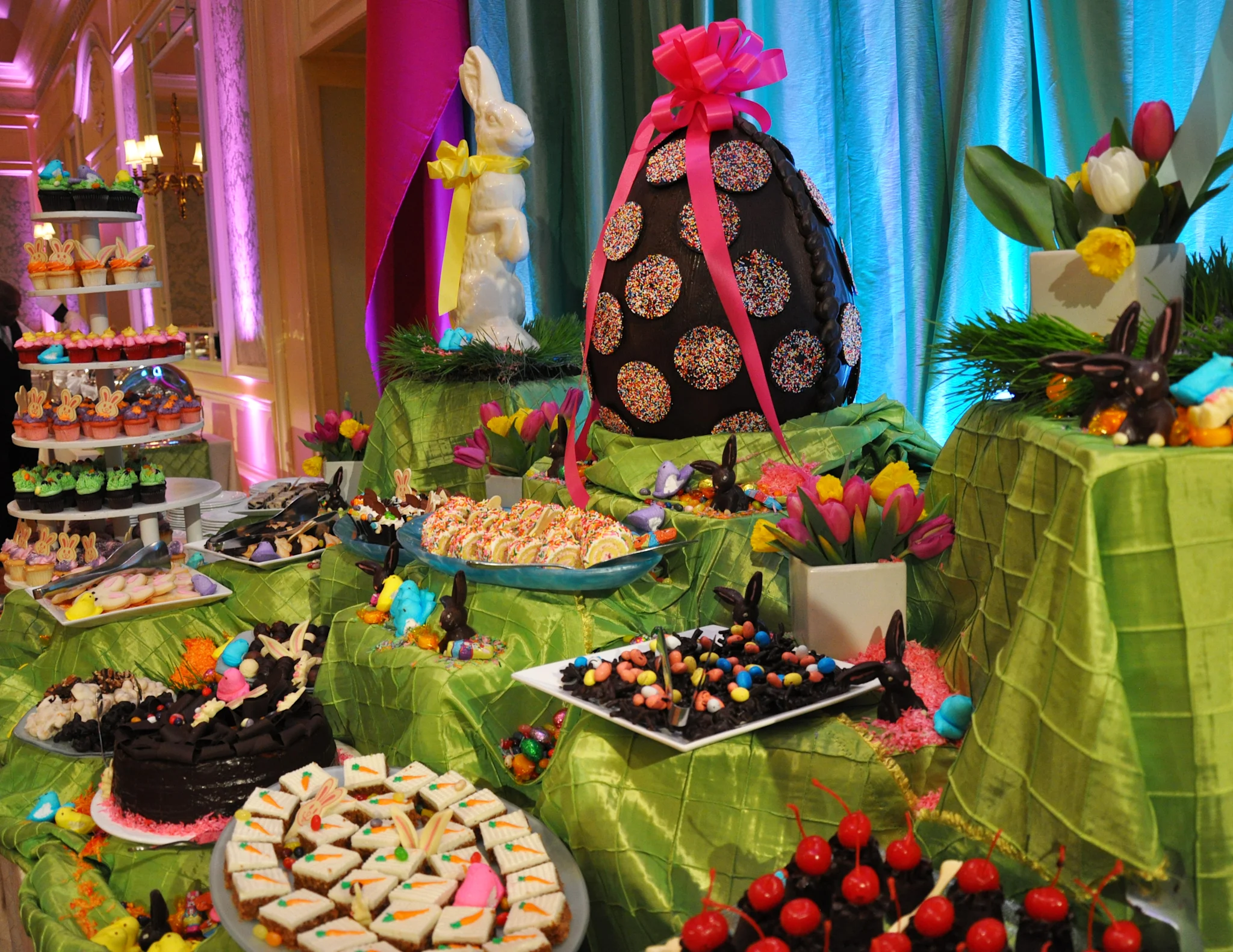 Colorful Easter dessert buffet with chocolate egg centerpiece, spring flowers, and assorted treats.