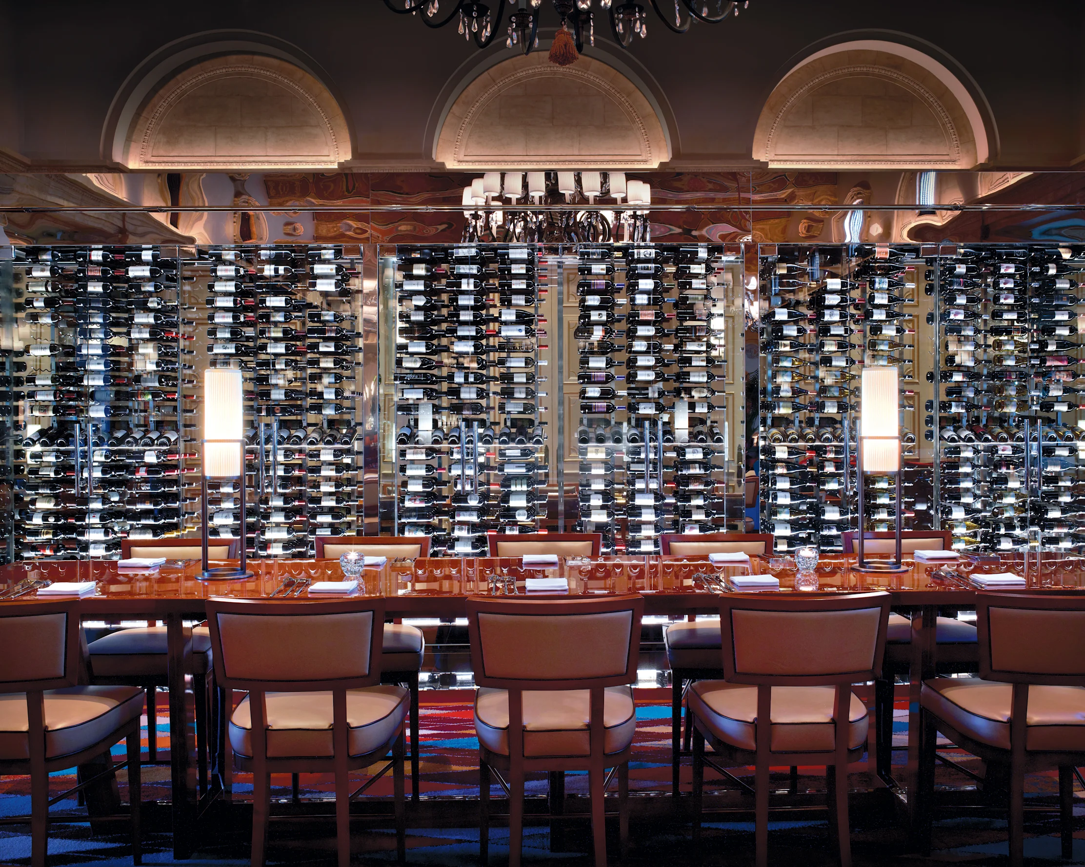 Elegant restaurant dining room with floor-to-ceiling wine bottle display and arched architectural details.
