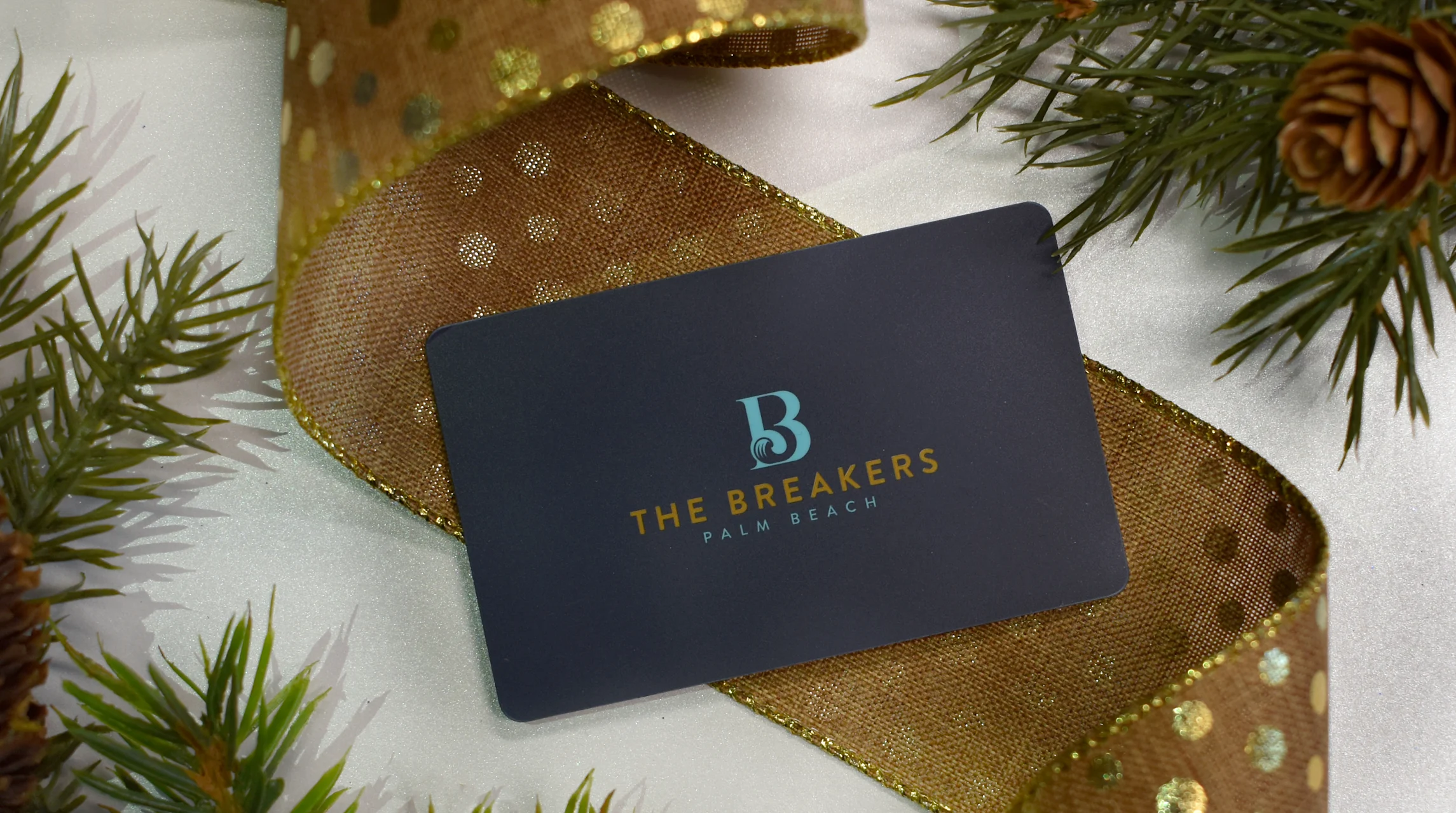 A Breakers Palm Beach gift card resting on a gold ribbon and pine branches.
