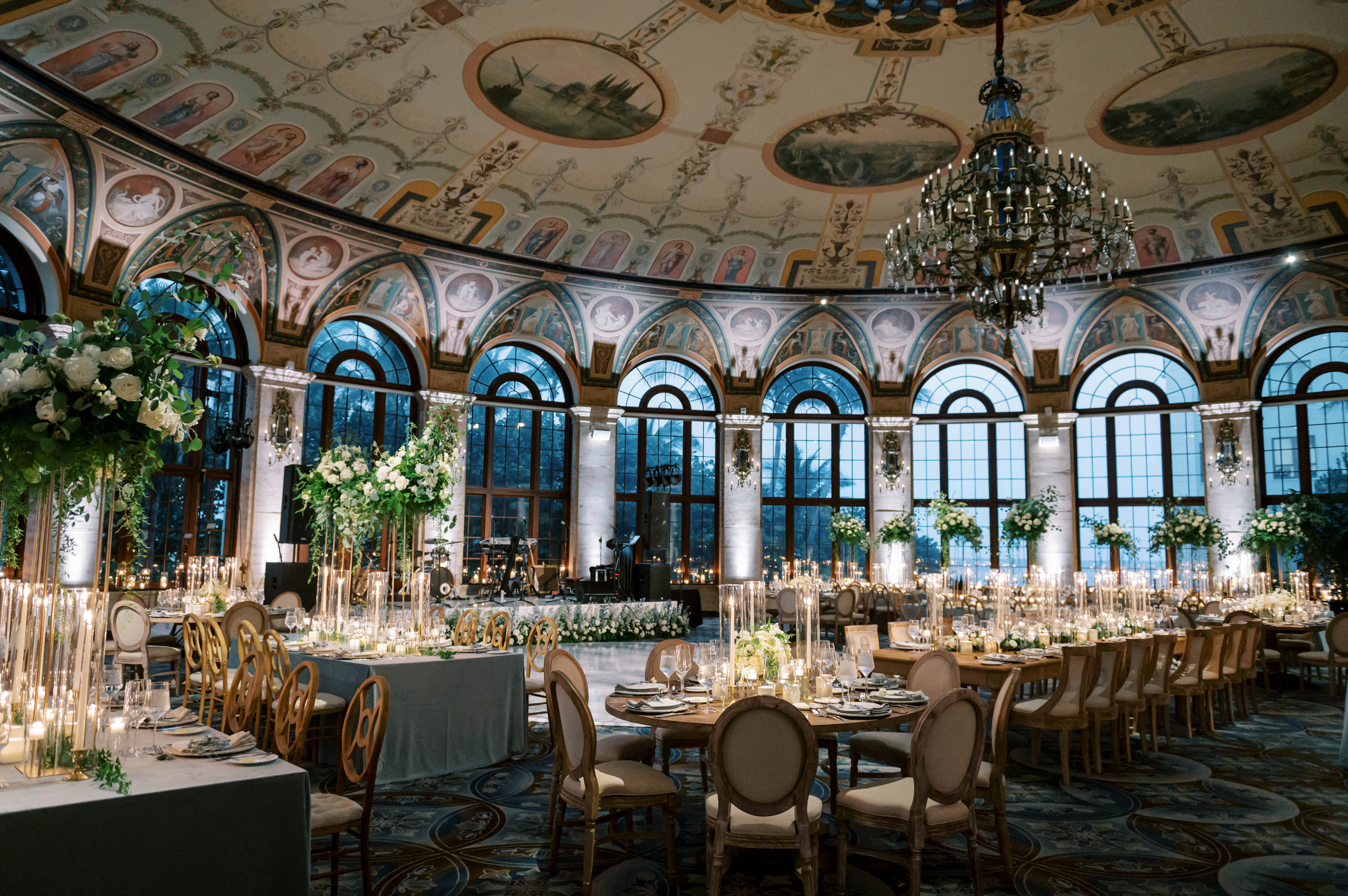 Elegant ballroom with ornate frescoed ceiling, crystal chandelier, arched windows, and formal dining tables.