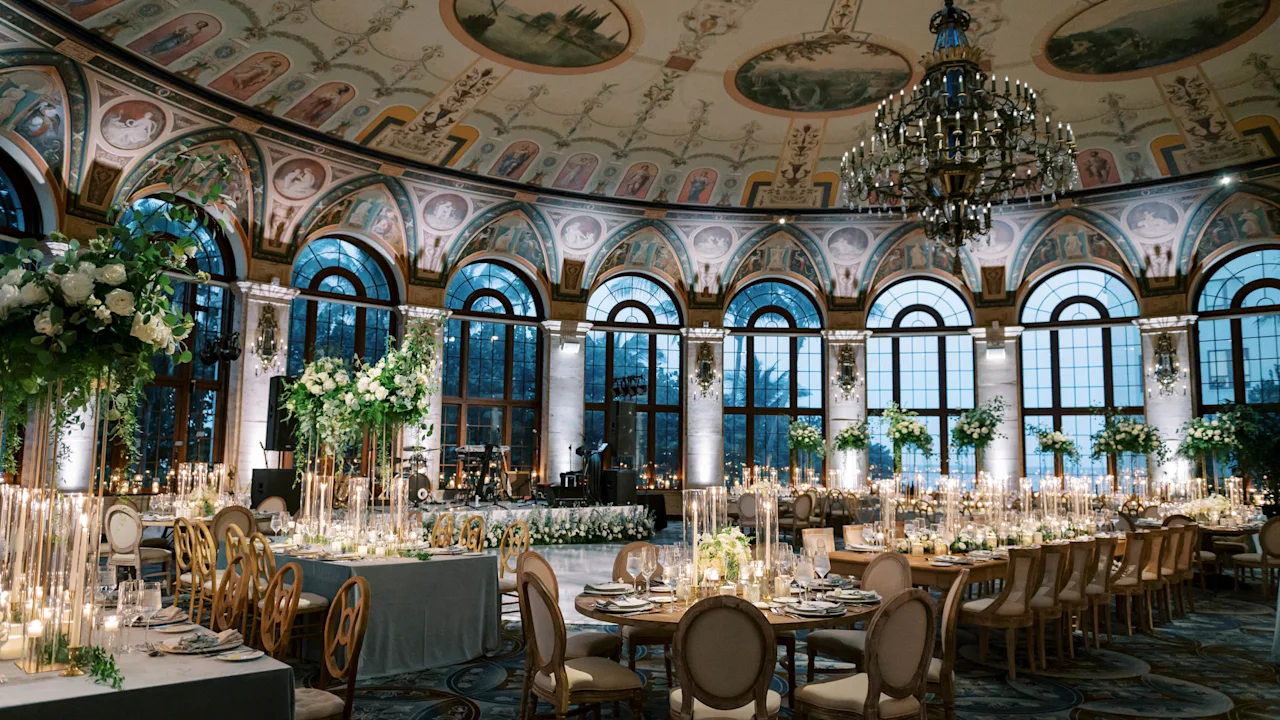 Elegant ballroom with ornate frescoed ceiling, crystal chandelier, arched windows, and formal dining tables.
