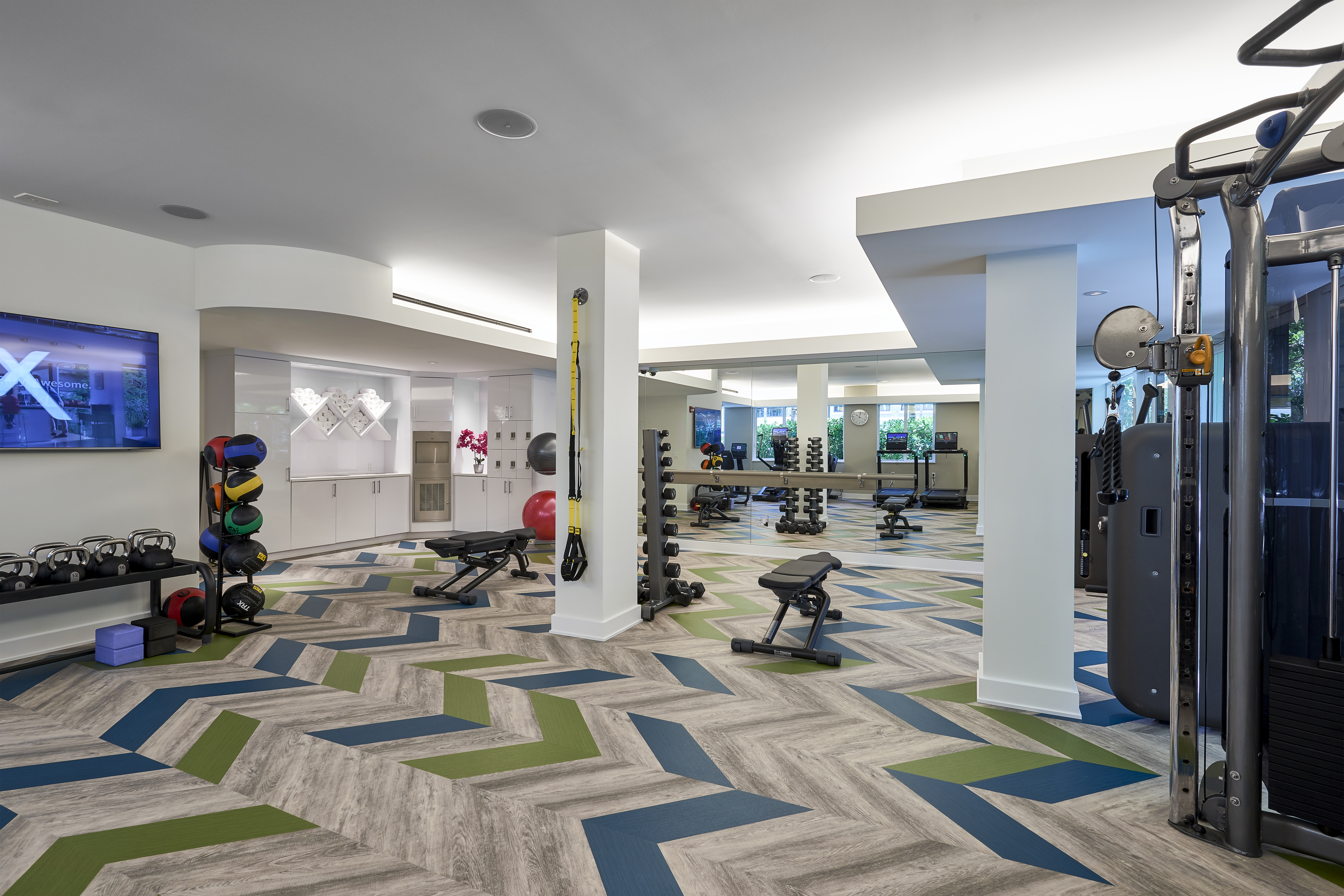 Modern fitness center with colorful geometric flooring, exercise equipment, and white columns.