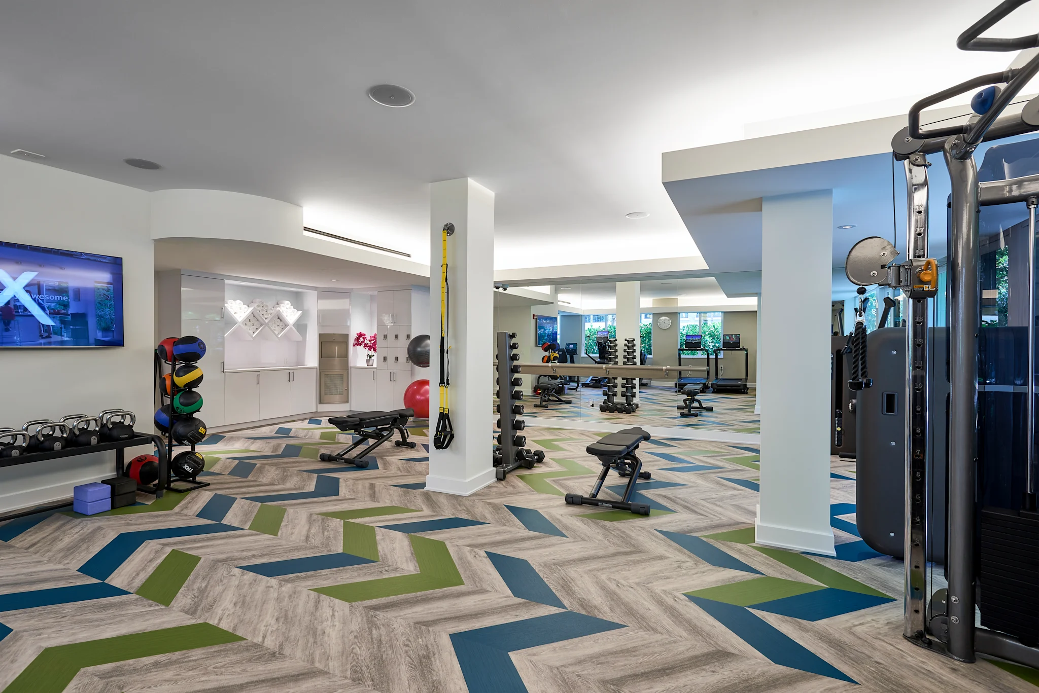 Modern fitness center with colorful geometric flooring, exercise equipment, and white columns.