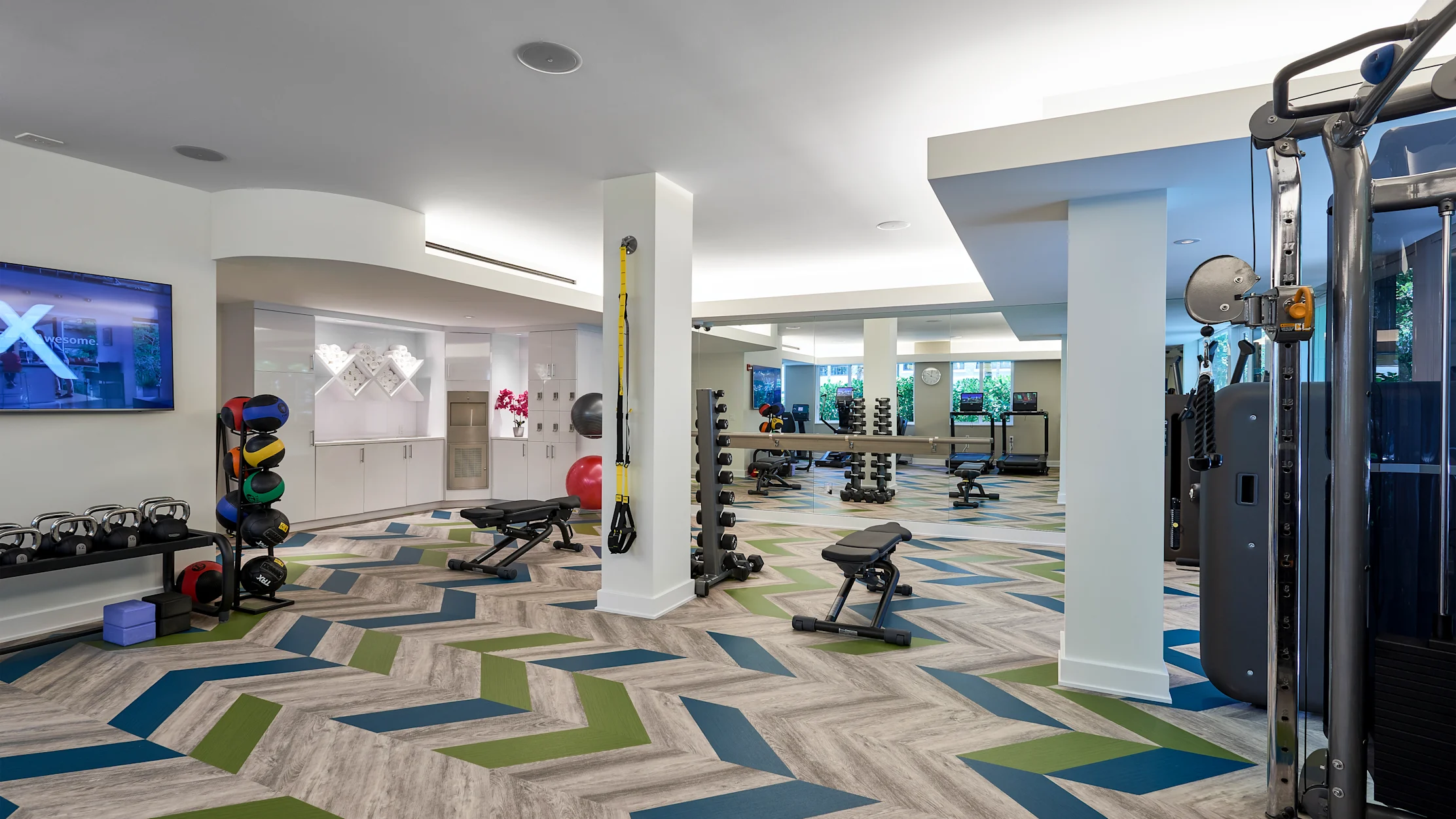 Modern fitness center with colorful geometric flooring, exercise equipment, and white columns.