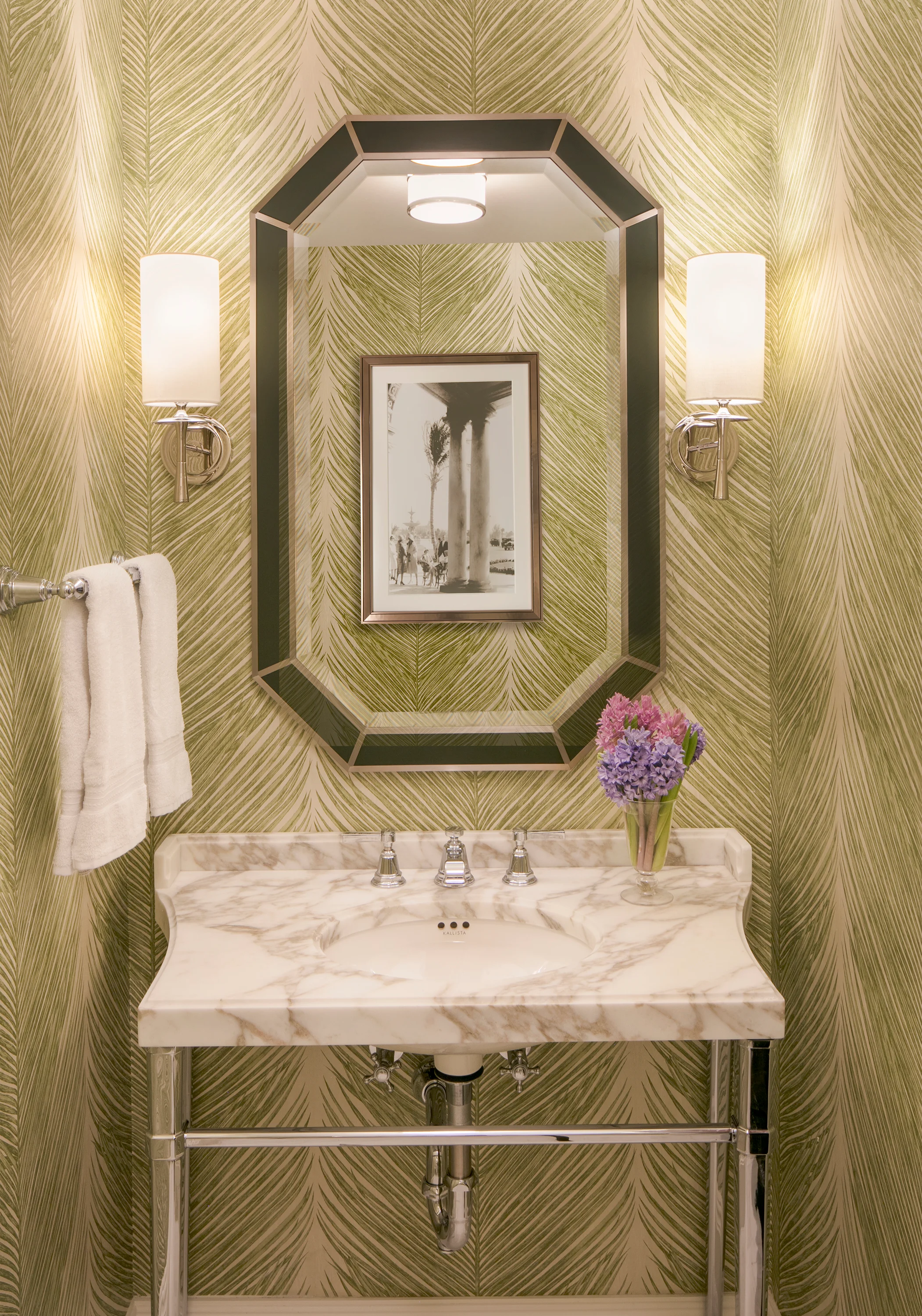 Elegant powder room with gold palm leaf wallpaper, octagonal mirror, marble vanity, and wall sconces.