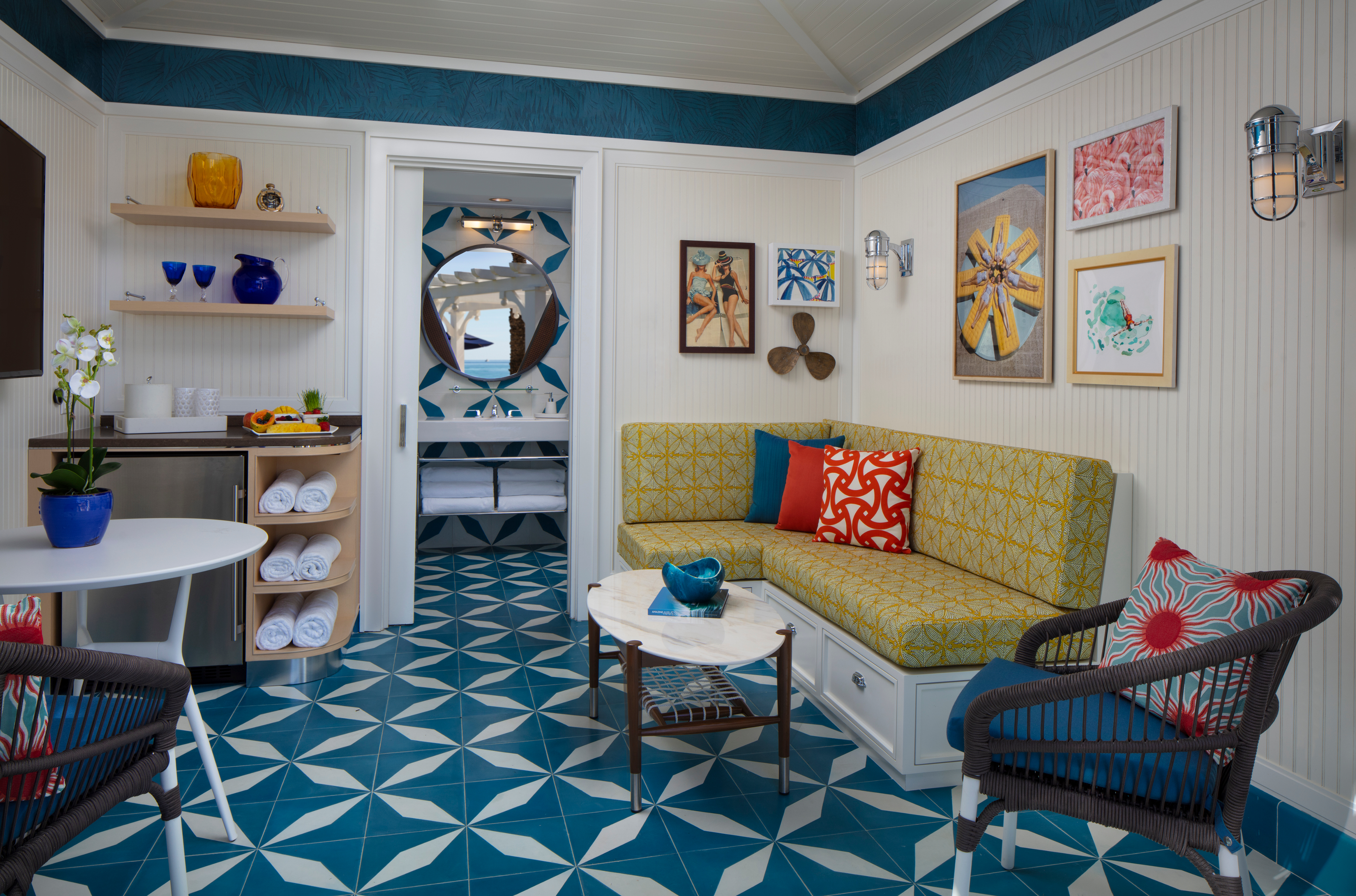 Bright coastal-themed room with yellow patterned sofa, teal geometric floor tiles, and nautical art.