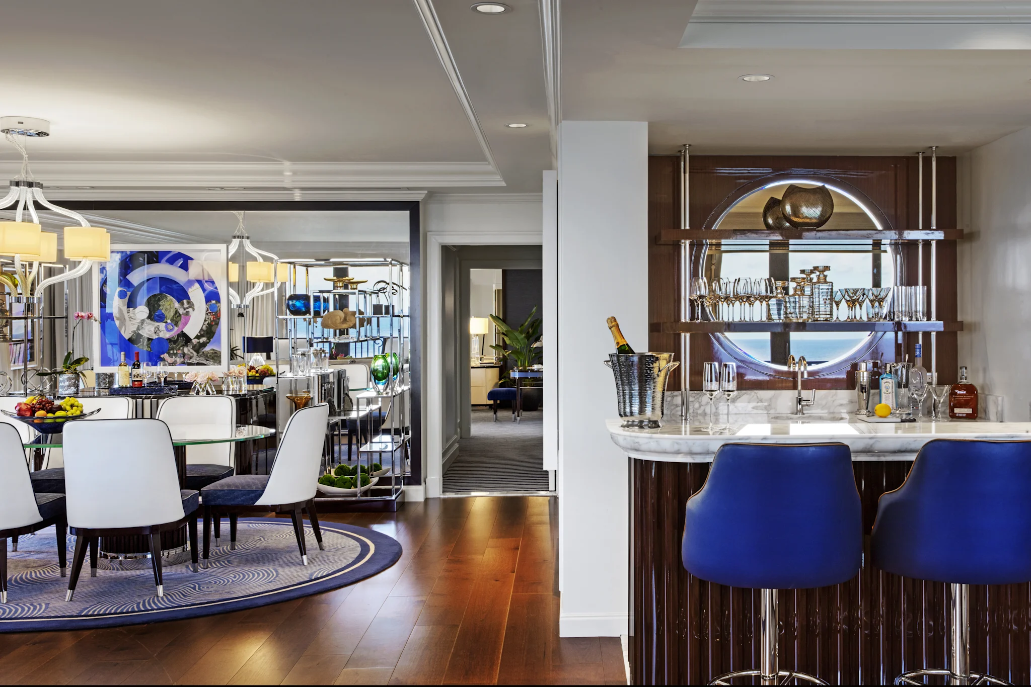 Luxury dining room with white chairs, blue artwork, and elegant bar with blue stools and champagne.