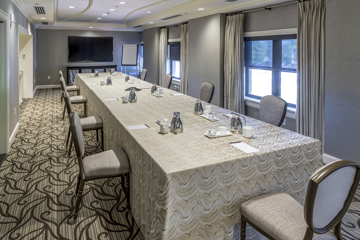 Conference room with U-shaped table, gray walls, patterned carpet, and windows with curtains.