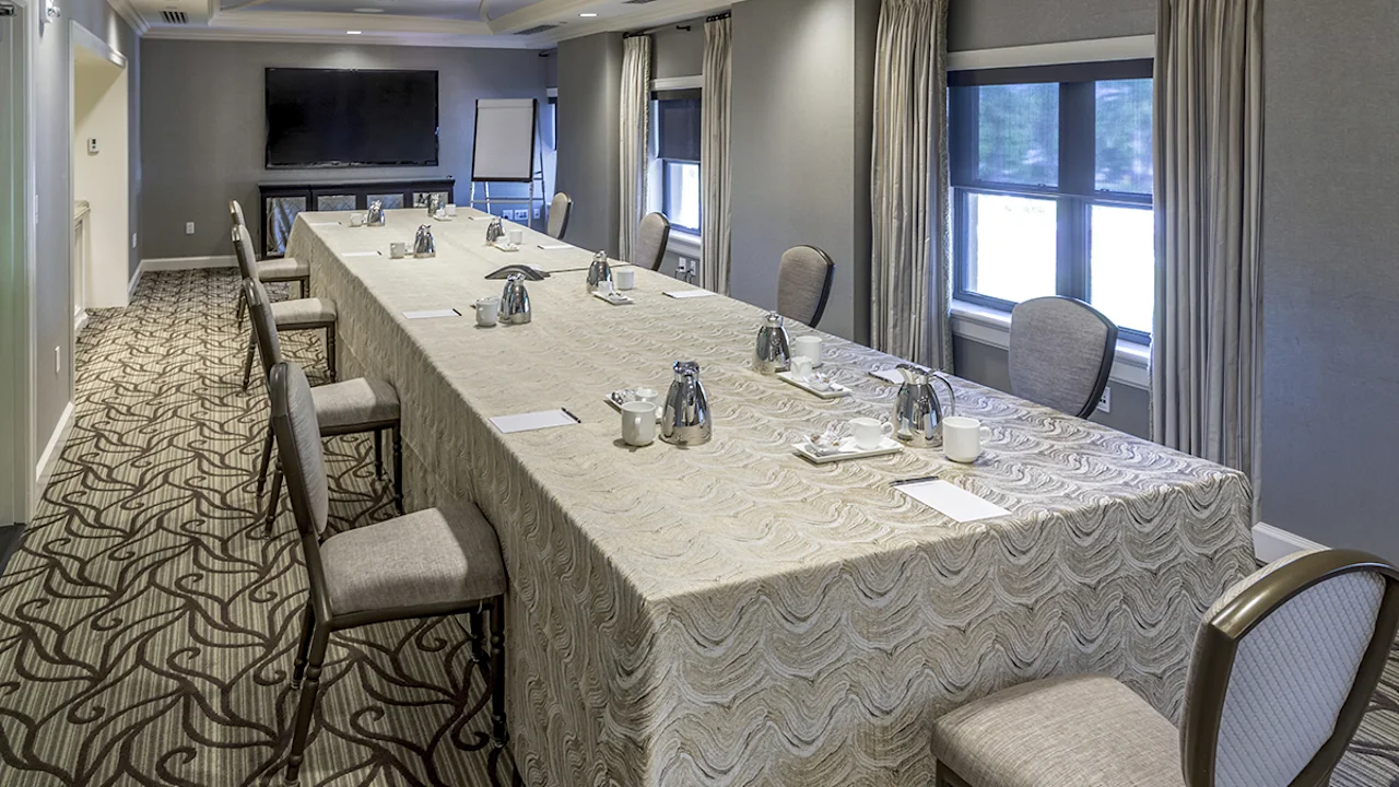 Conference room with U-shaped table, gray walls, patterned carpet, and windows with curtains.