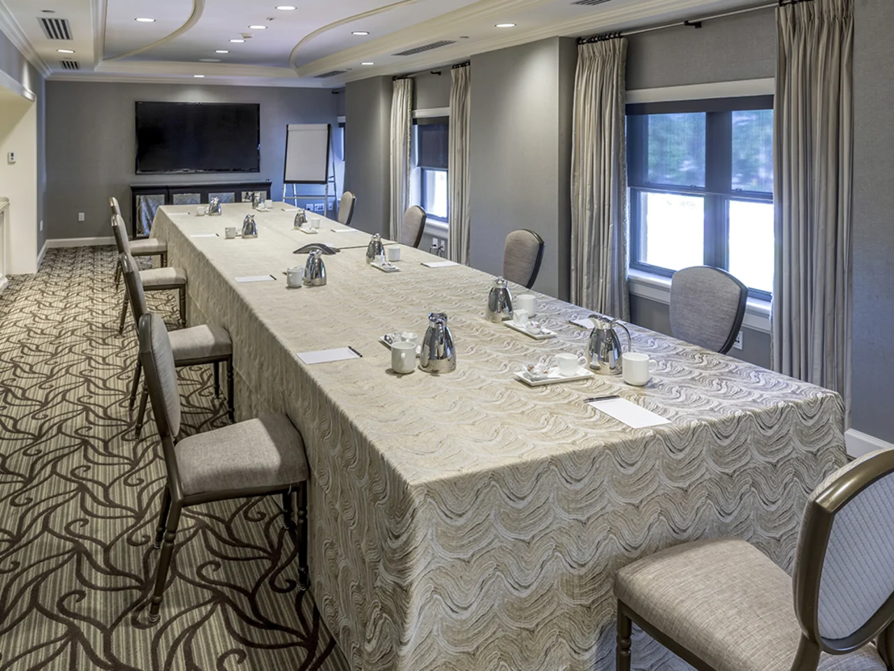 Conference room with U-shaped table, gray walls, patterned carpet, and windows with curtains.