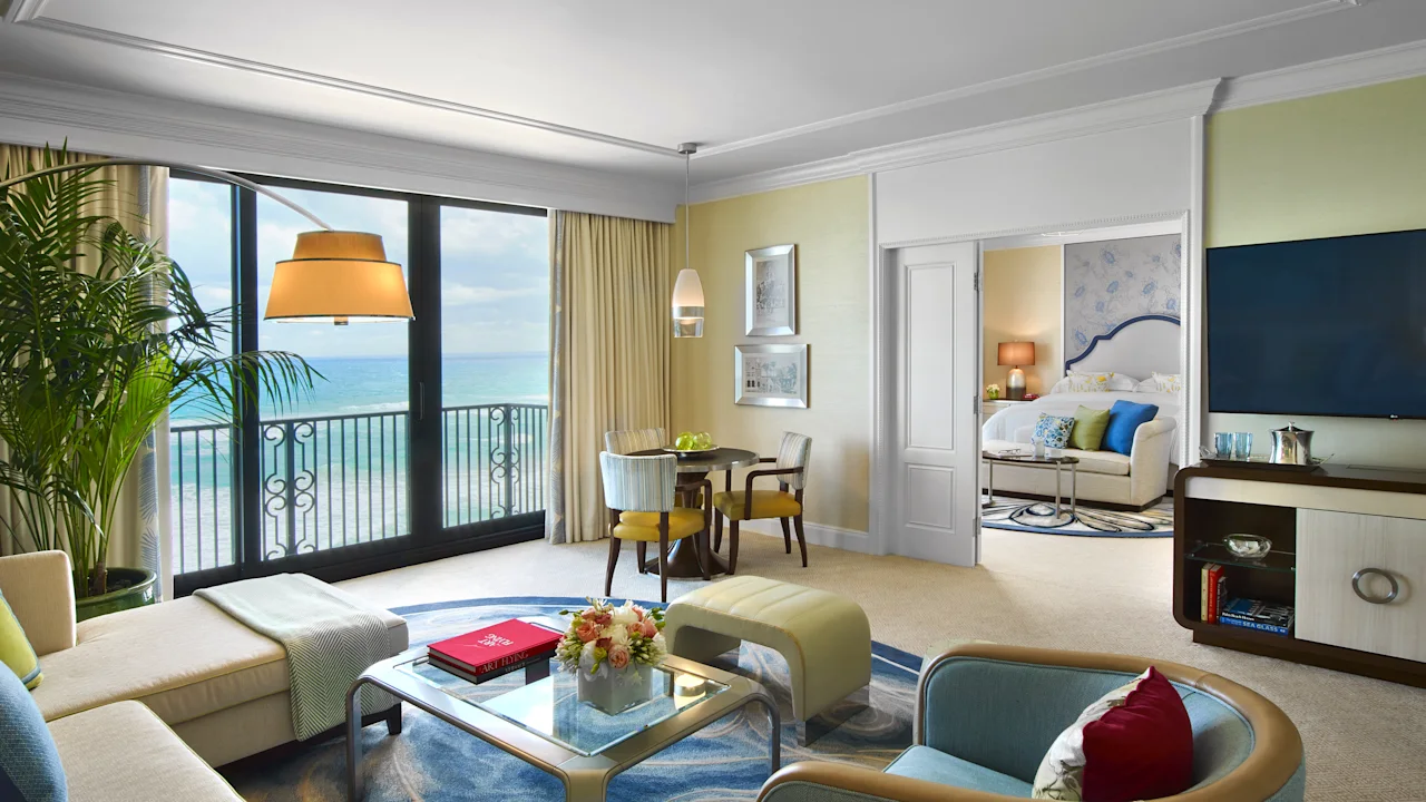 Luxury hotel suite with ocean view, featuring modern furniture, yellow and blue accents, and balcony.