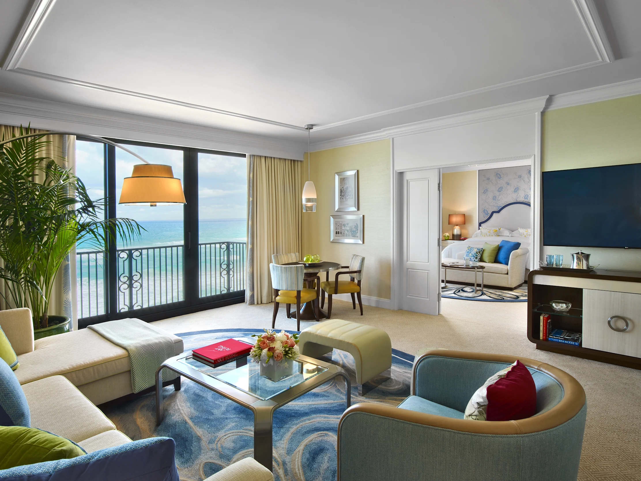 Luxury hotel suite with ocean view, featuring modern furniture, yellow and blue accents, and balcony.