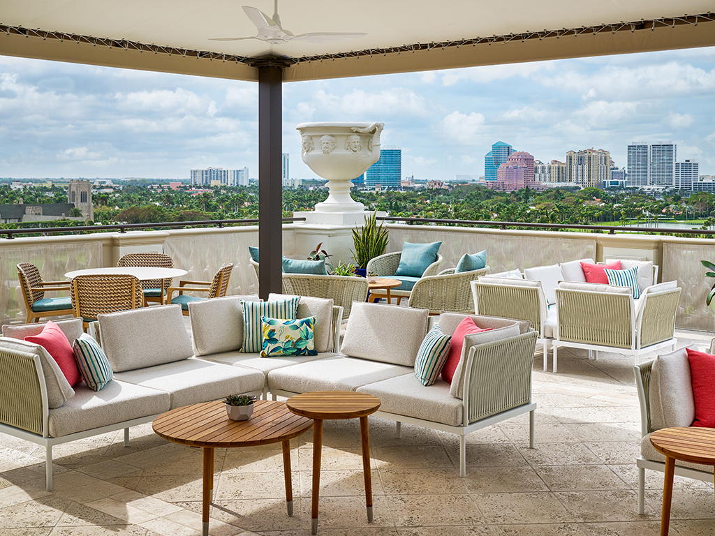 Rooftop terrace with beige sofas, colorful pillows, and city skyline view under covered patio.