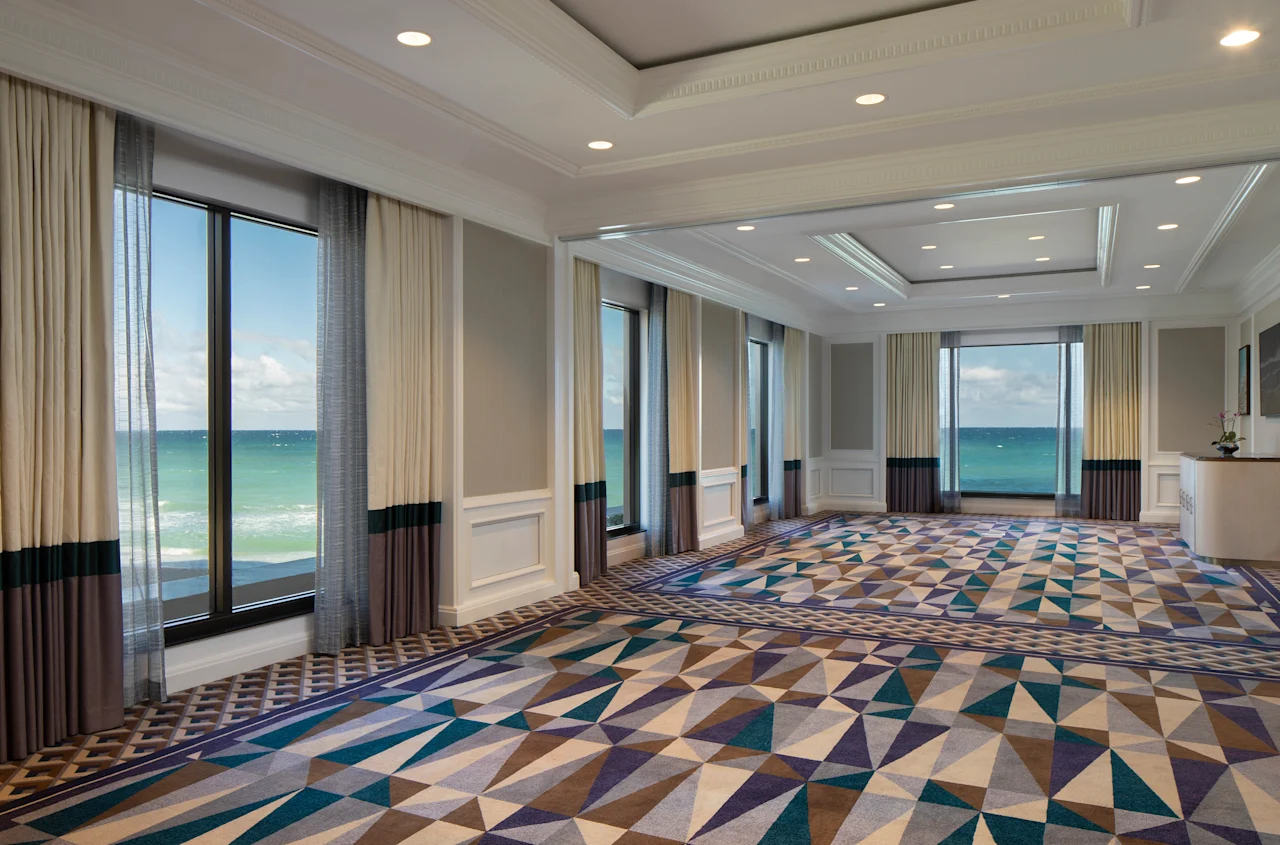 Elegant ballroom with geometric patterned carpet, floor-to-ceiling windows, and ocean views.