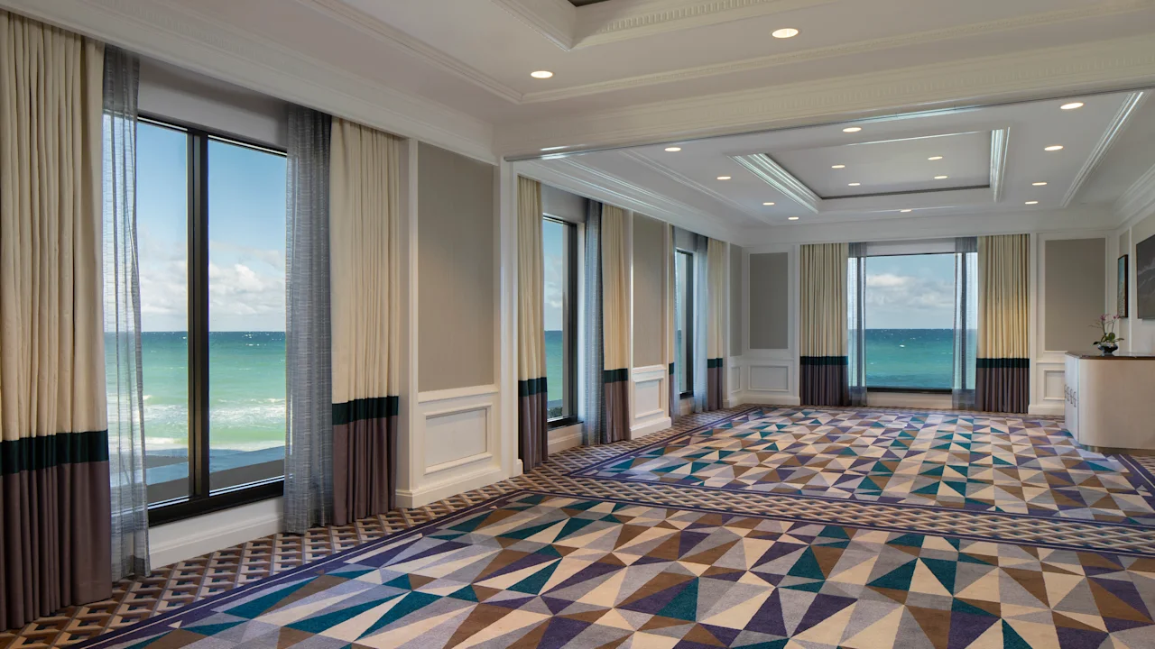 Elegant ballroom with geometric patterned carpet, floor-to-ceiling windows, and ocean views.