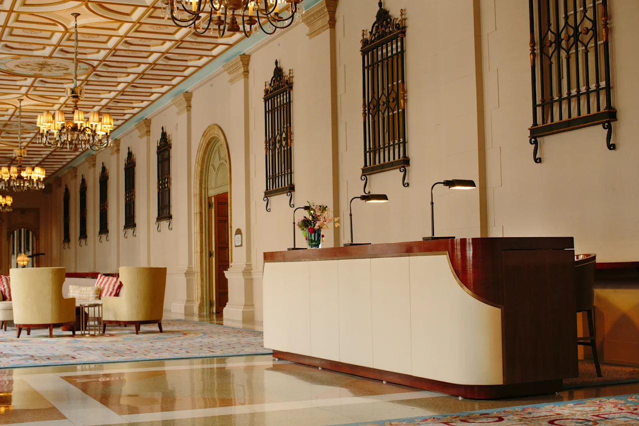Elegant hotel lobby with ornate ceiling, chandeliers, decorative wall panels, and modern reception desk