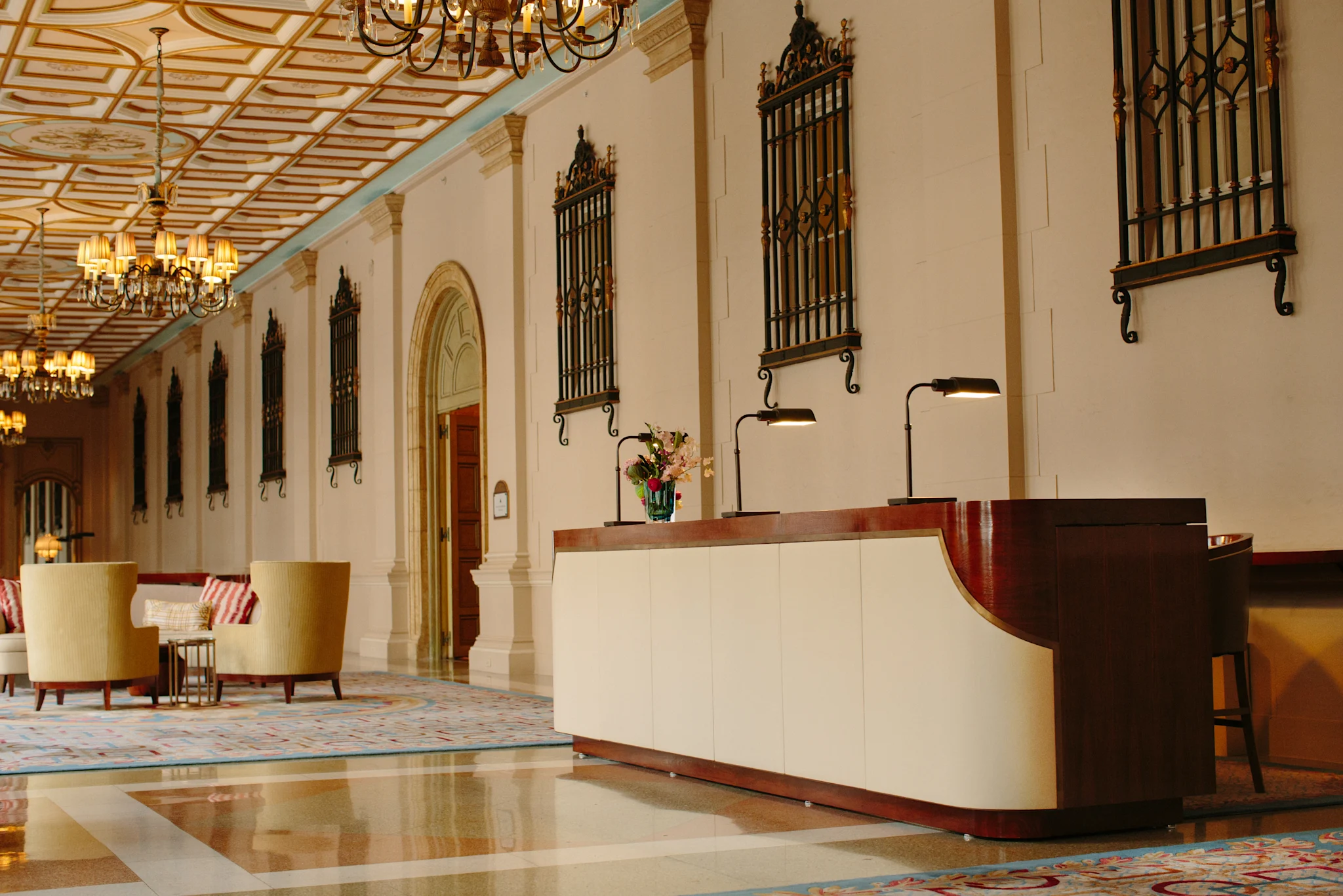 Elegant hotel lobby with ornate ceiling, chandeliers, decorative wall panels, and modern reception desk