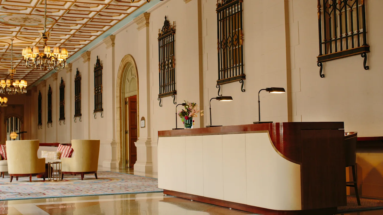 Elegant hotel lobby with ornate ceiling, chandeliers, decorative wall panels, and modern reception desk