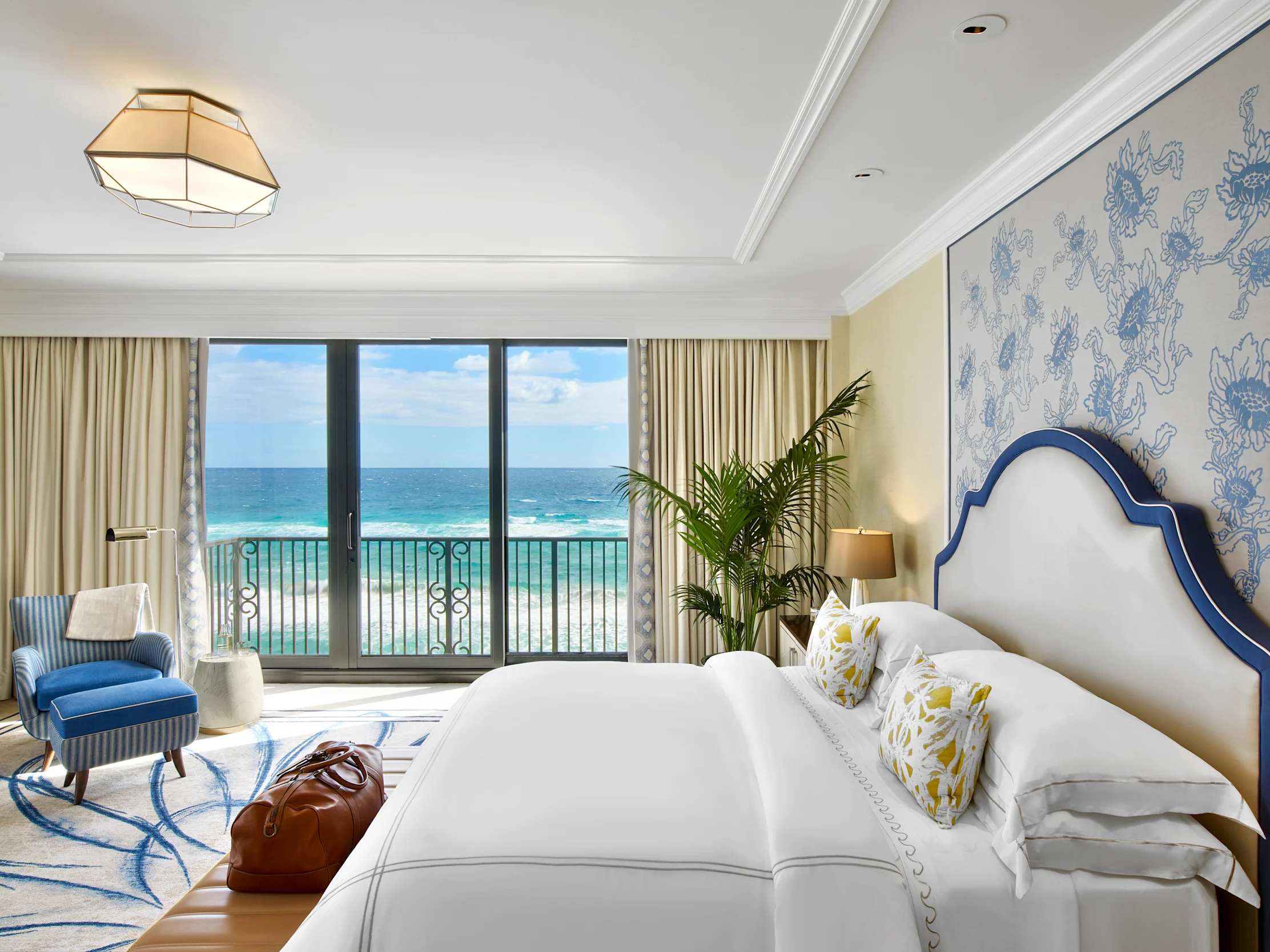 Elegant hotel bedroom with ocean view, white bedding, blue accents, and coastal decor.