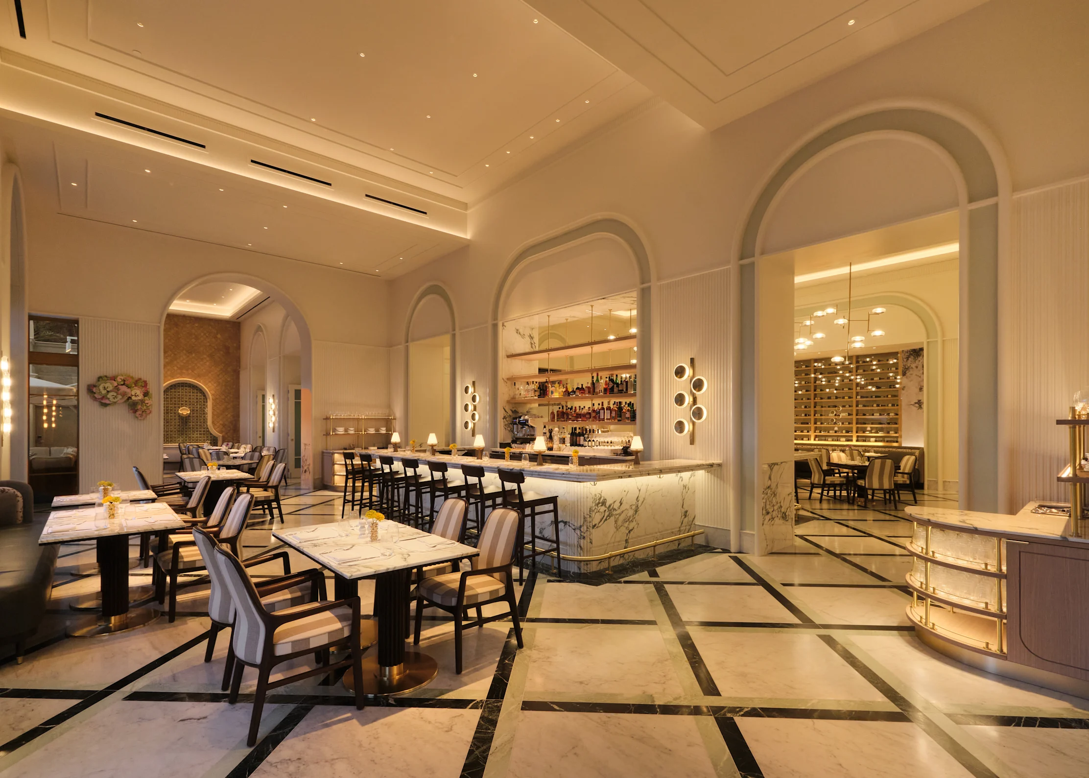 Elegant restaurant interior with tan and blue patterned chairs, wood tables, arched windows, and ocean view.