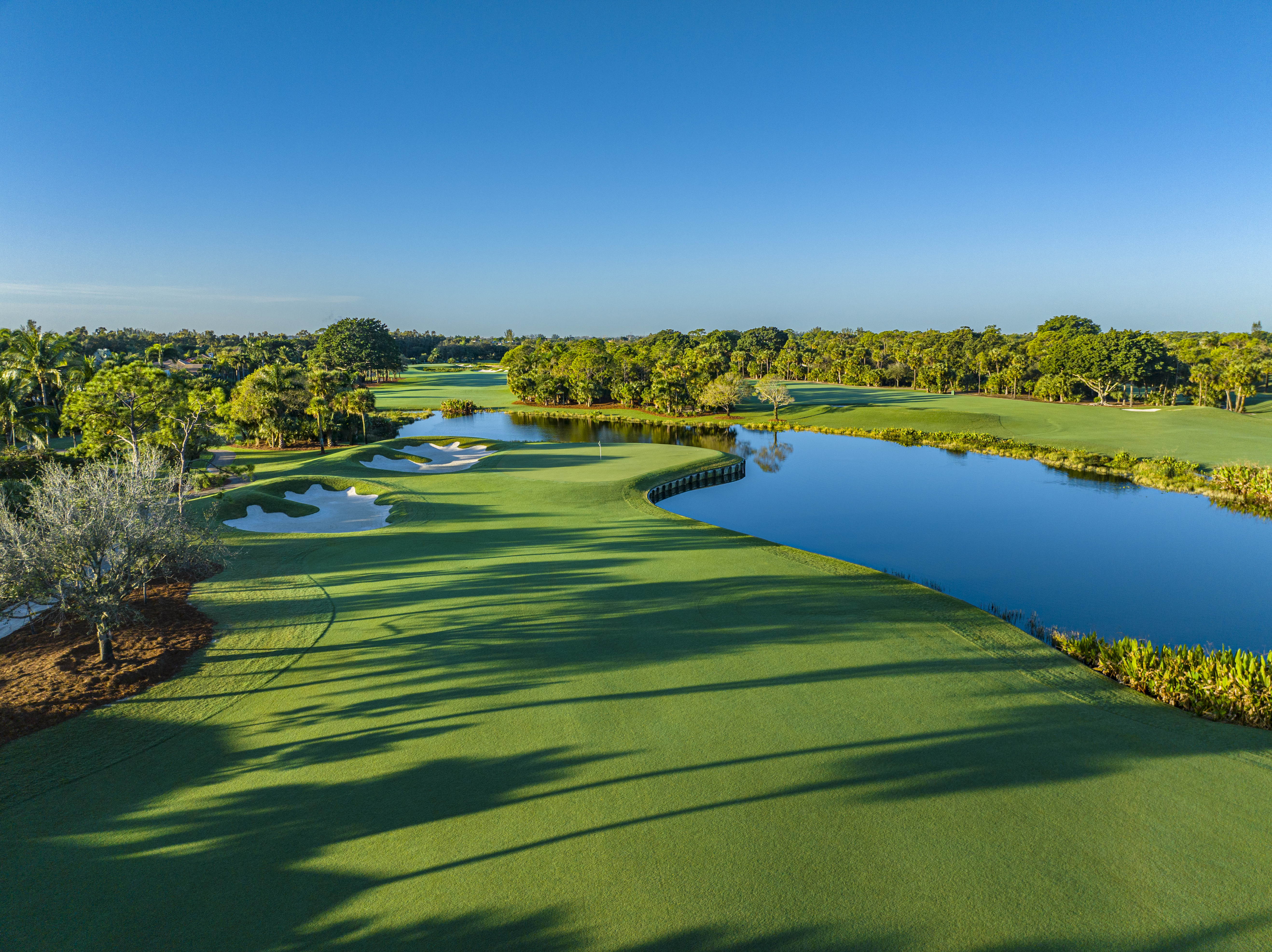 Scenic golf course with lush green fairways, blue water hazards, and trees under a clear sky.