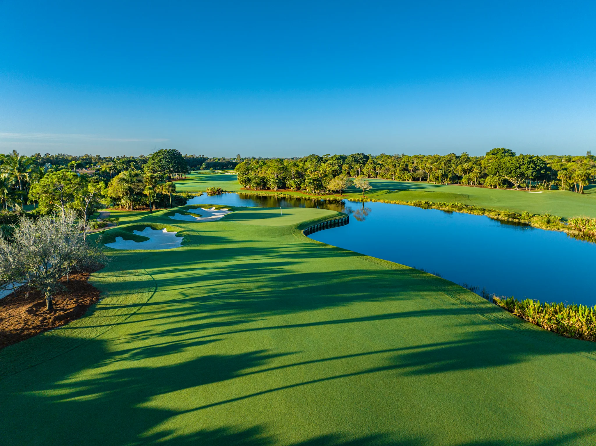 Scenic golf course with lush green fairways, blue water hazards, and trees under a clear sky.