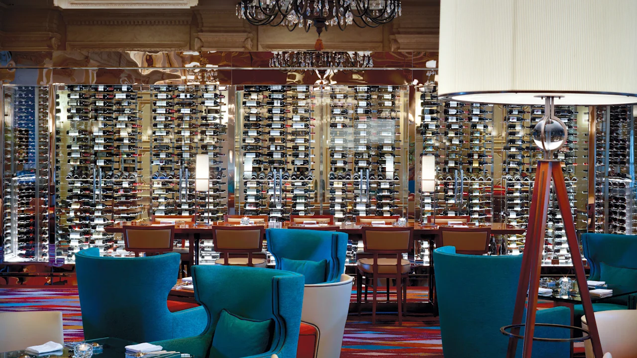 Elegant restaurant interior with turquoise chairs, large white lampshade, chandelier, and illuminated wine cellar wall display.