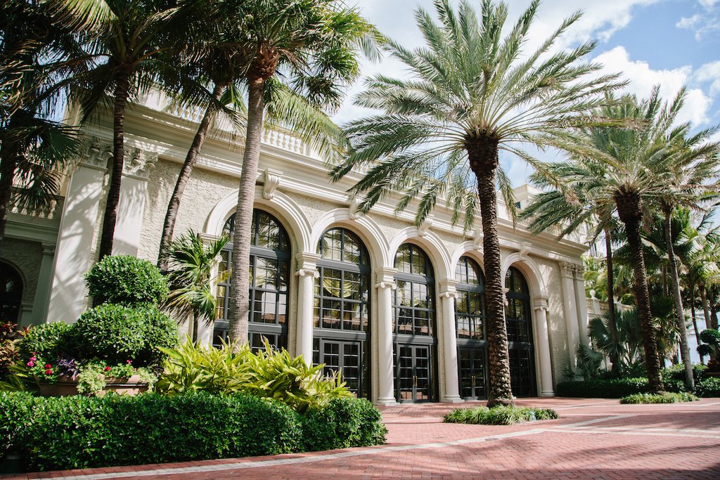 Elegant white building with arched entrances surrounded by palm trees and lush tropical landscaping.