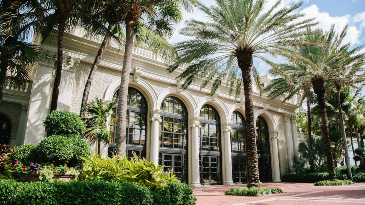 Elegant white building with arched entrances surrounded by palm trees and lush tropical landscaping.