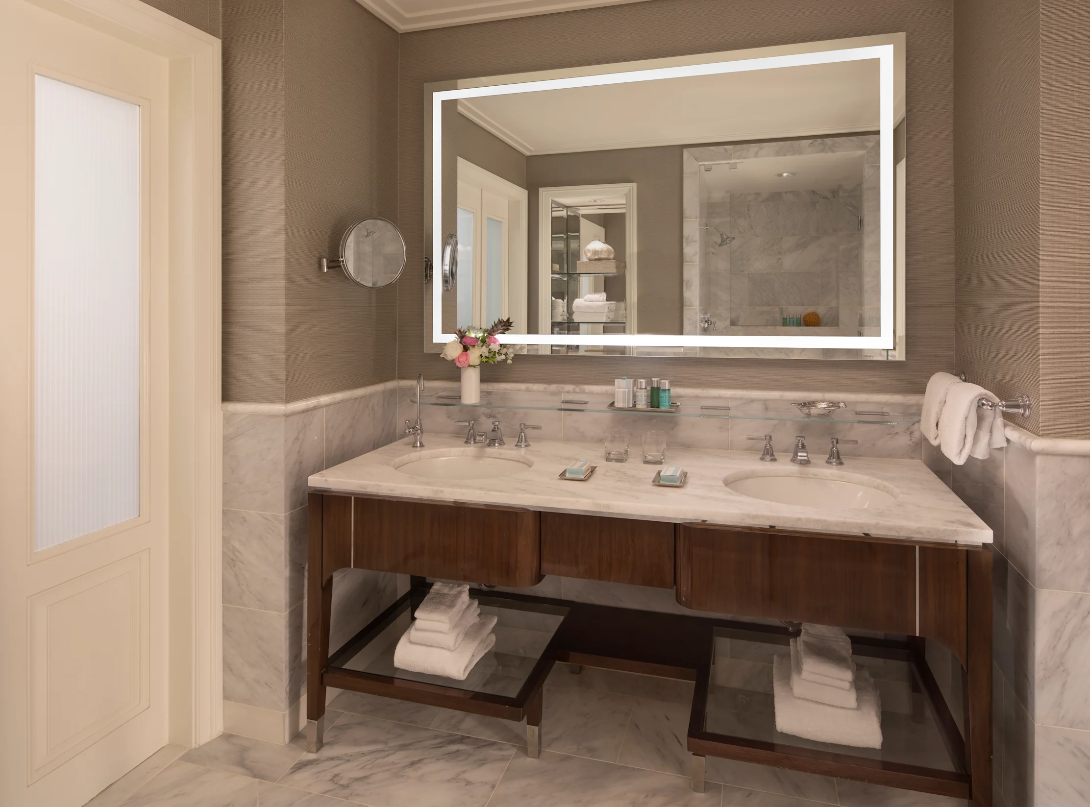 Modern bathroom with double marble vanity, LED-lit mirror, wood cabinets, and white towels.