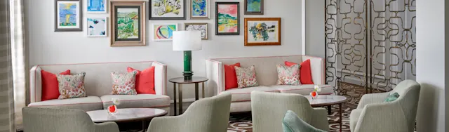 Bright living room with beige sofas, coral pillows, green chairs, and colorful framed artwork on wall.