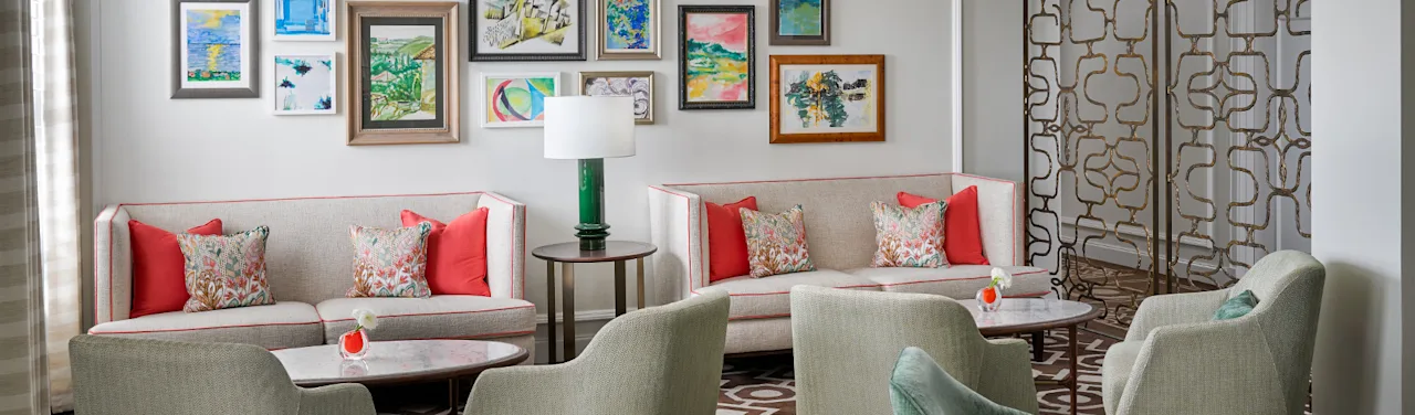 Bright living room with beige sofas, coral pillows, green chairs, and colorful framed artwork on wall.
