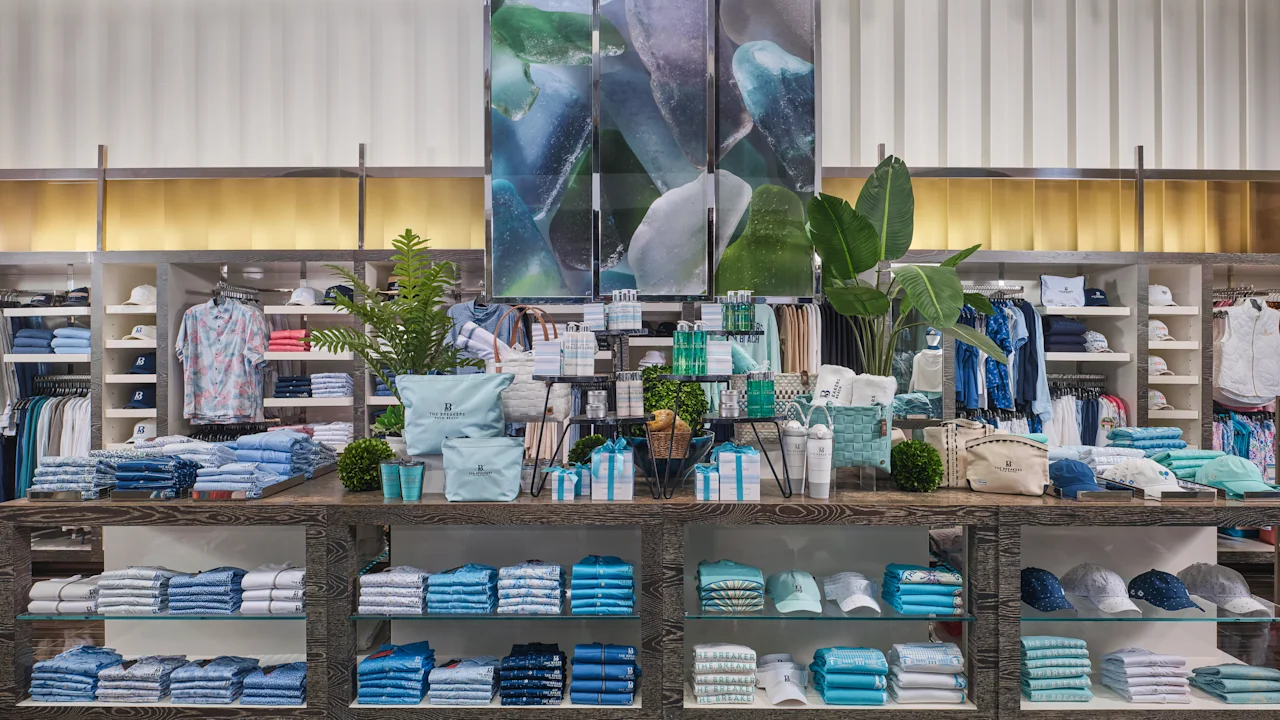 Modern retail store interior with folded clothing in blue and white tones, plants, and sea glass artwork.