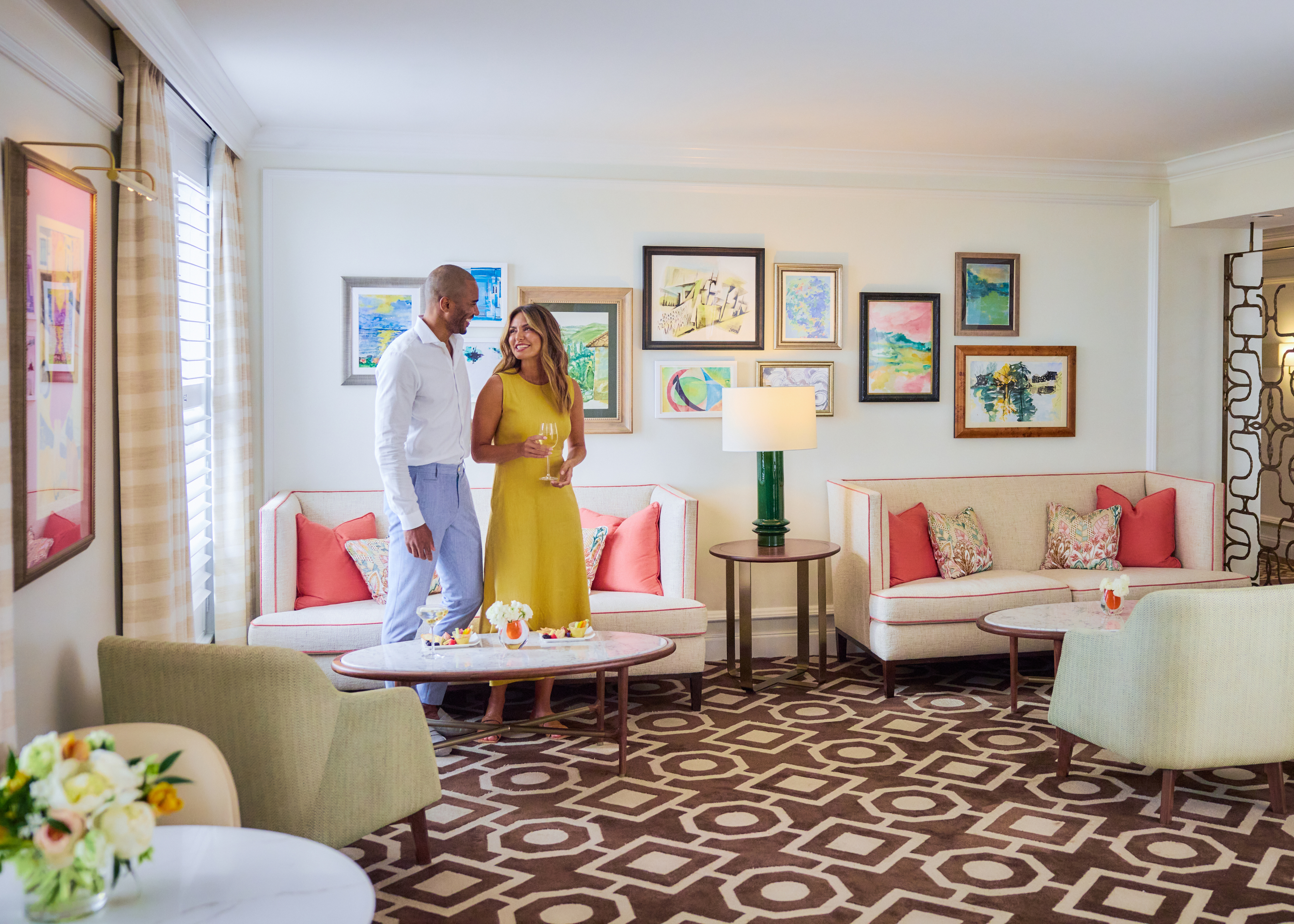 Couple in bright living room with gallery wall, coral accent pillows, and geometric patterned floor.