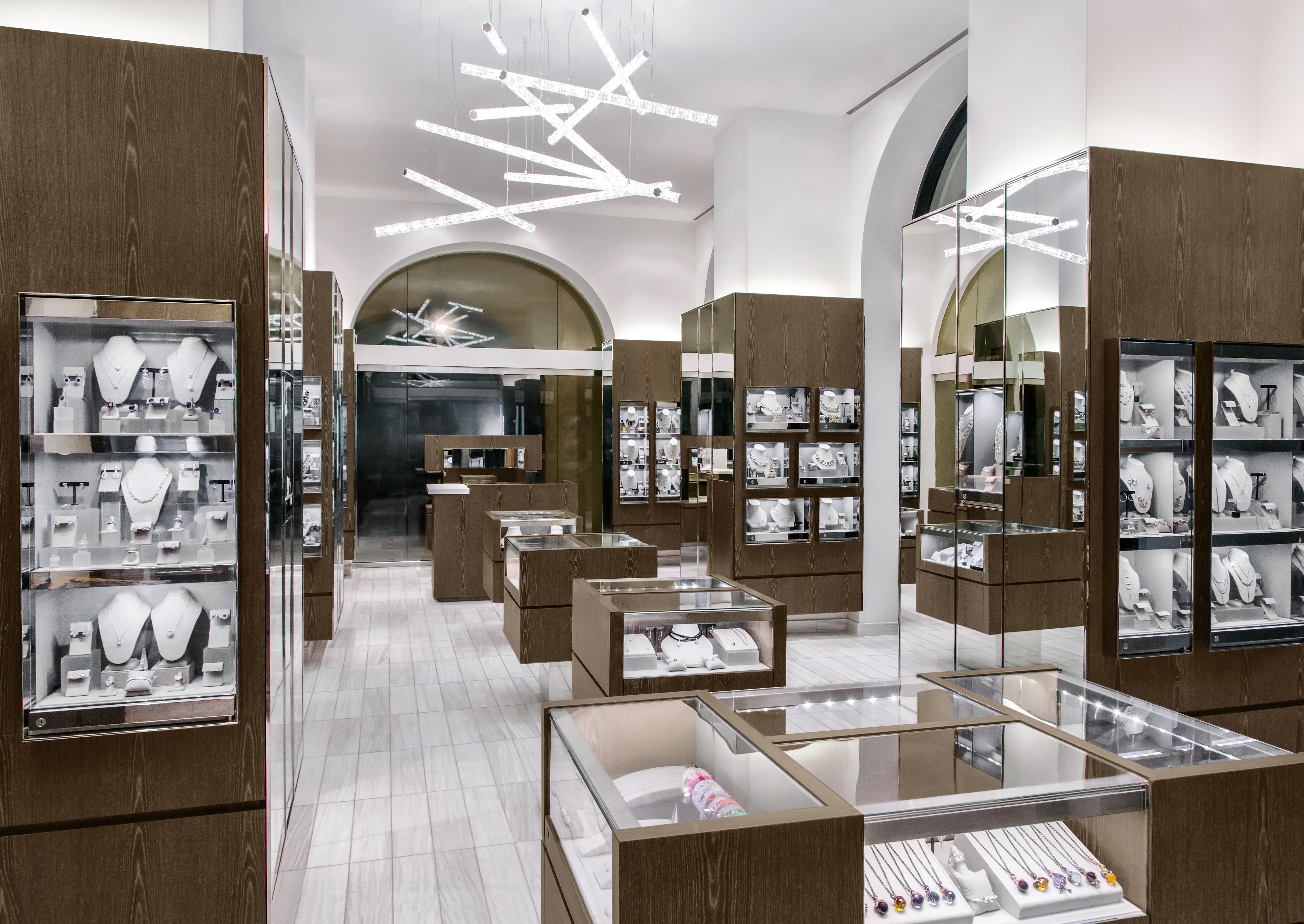 Modern jewelry store interior with wood and glass display cases, white walls, and geometric lighting.