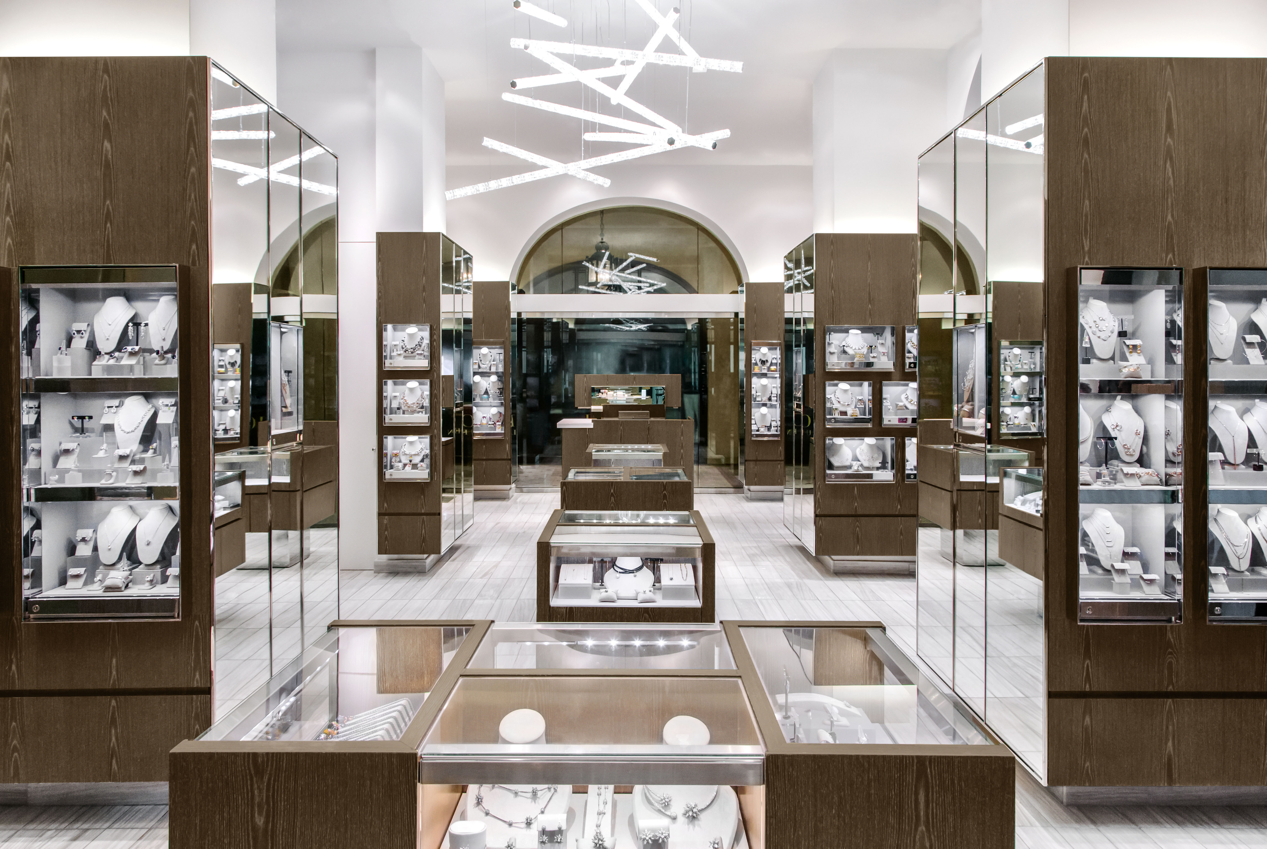 Modern jewelry store interior with wood and glass display cases, white walls, and geometric lighting.