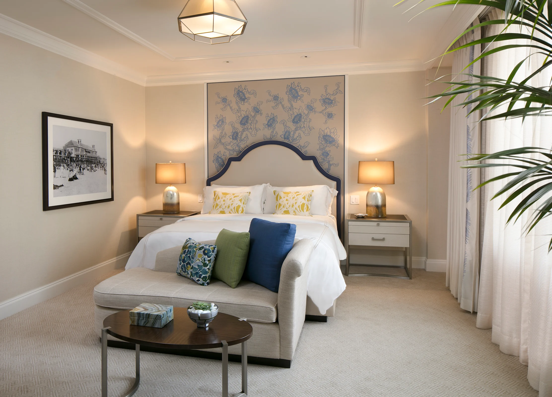 Elegant bedroom with blue upholstered headboard, white bedding, matching nightstands, and a settee.
