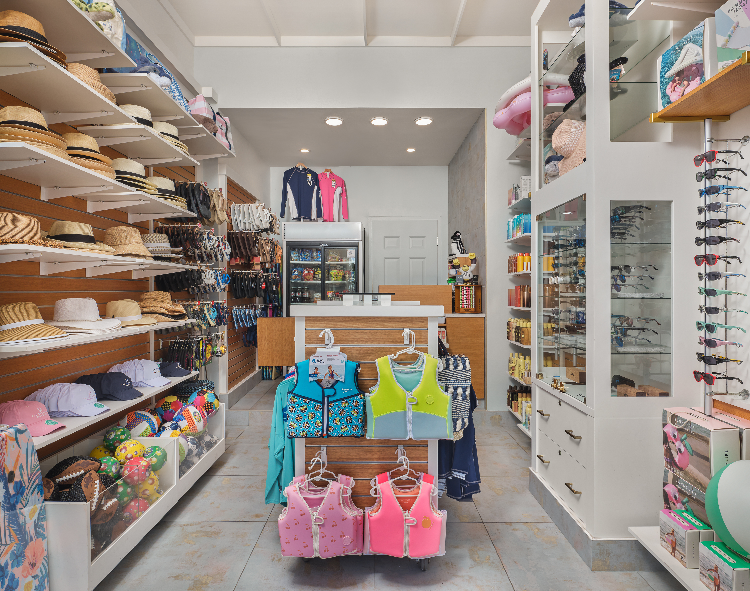 Bright retail store interior with hats, sunglasses, children's life vests, and beach accessories.
