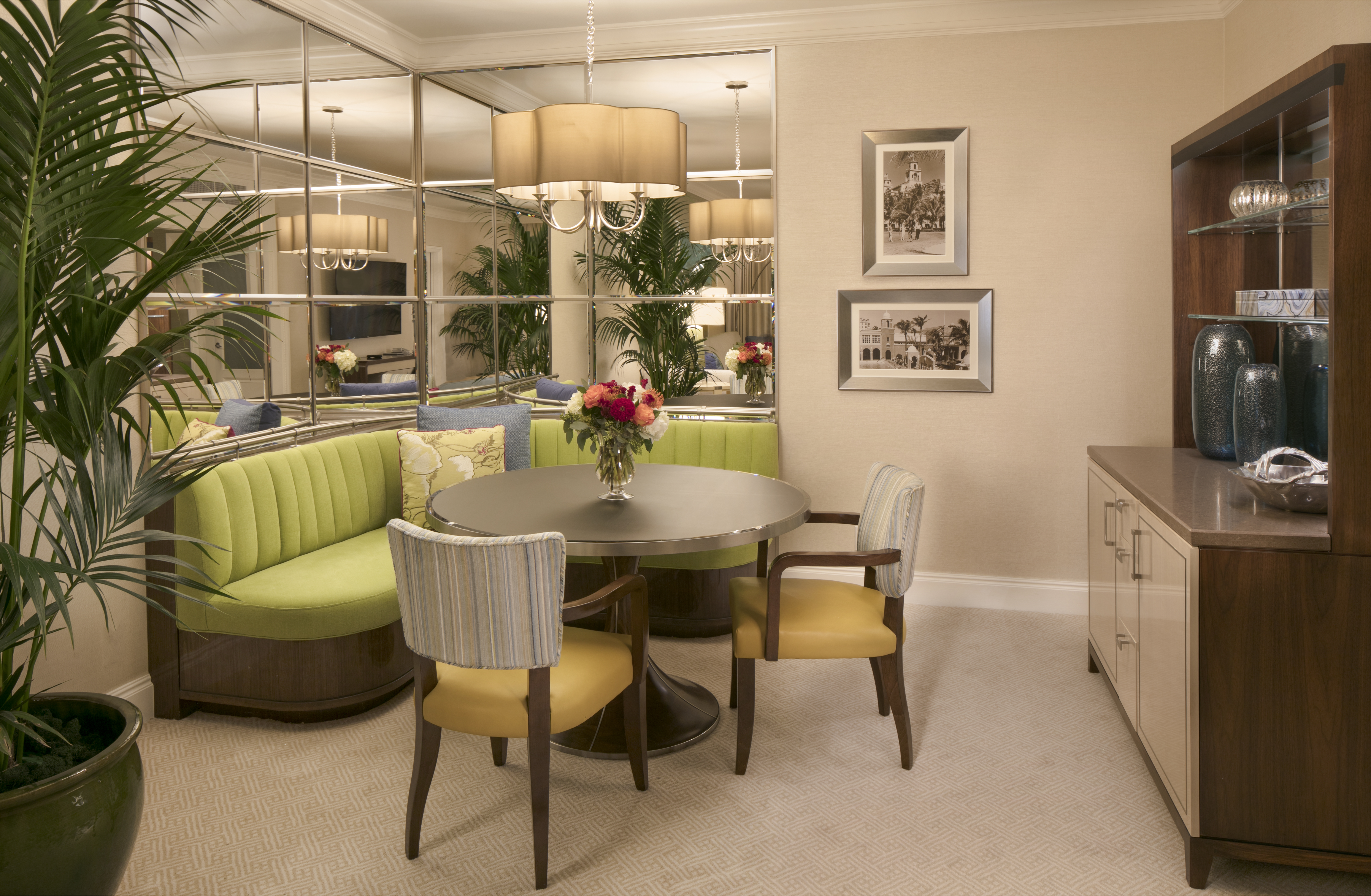 Elegant dining room with round table, lime green curved banquette, mirrored wall, and wooden cabinet.