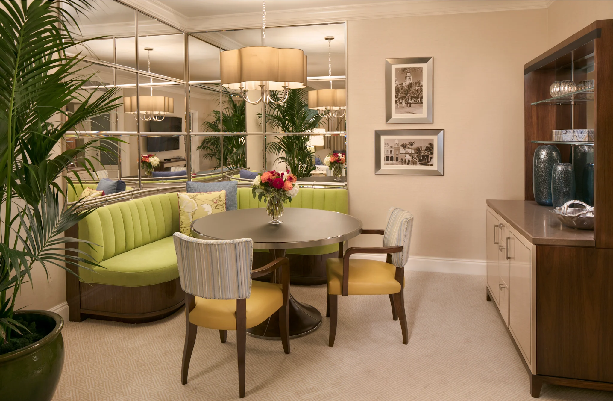 Elegant dining room with round table, lime green curved banquette, mirrored wall, and wooden cabinet.