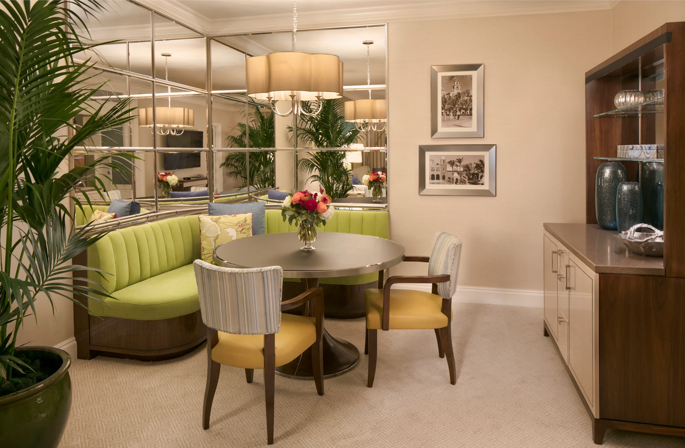 Elegant dining room with round table, lime green curved banquette, mirrored wall, and wooden cabinet.