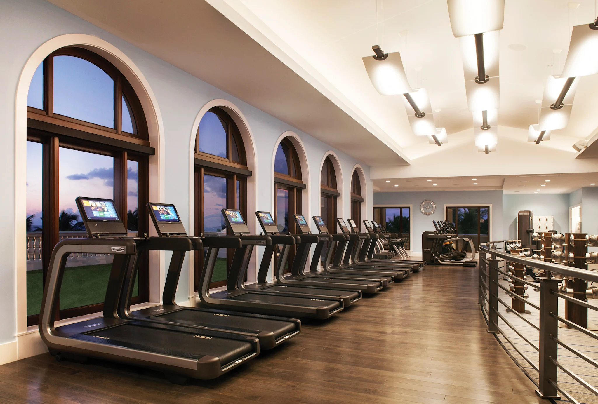 Modern fitness center with row of treadmills along arched windows and weight equipment area