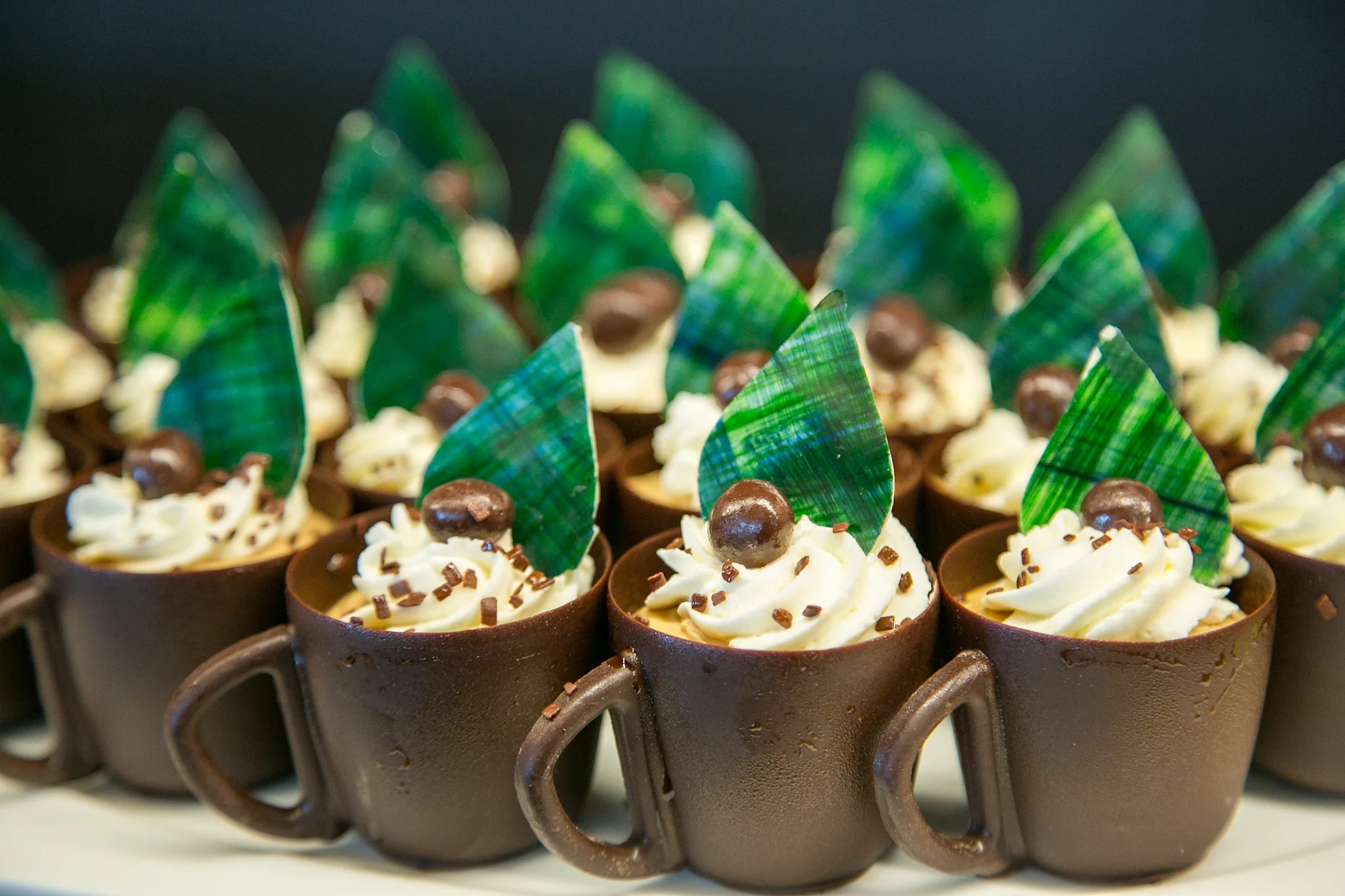 Chocolate cup desserts with white cream, green leaf garnish, and chocolate spheres on top.
