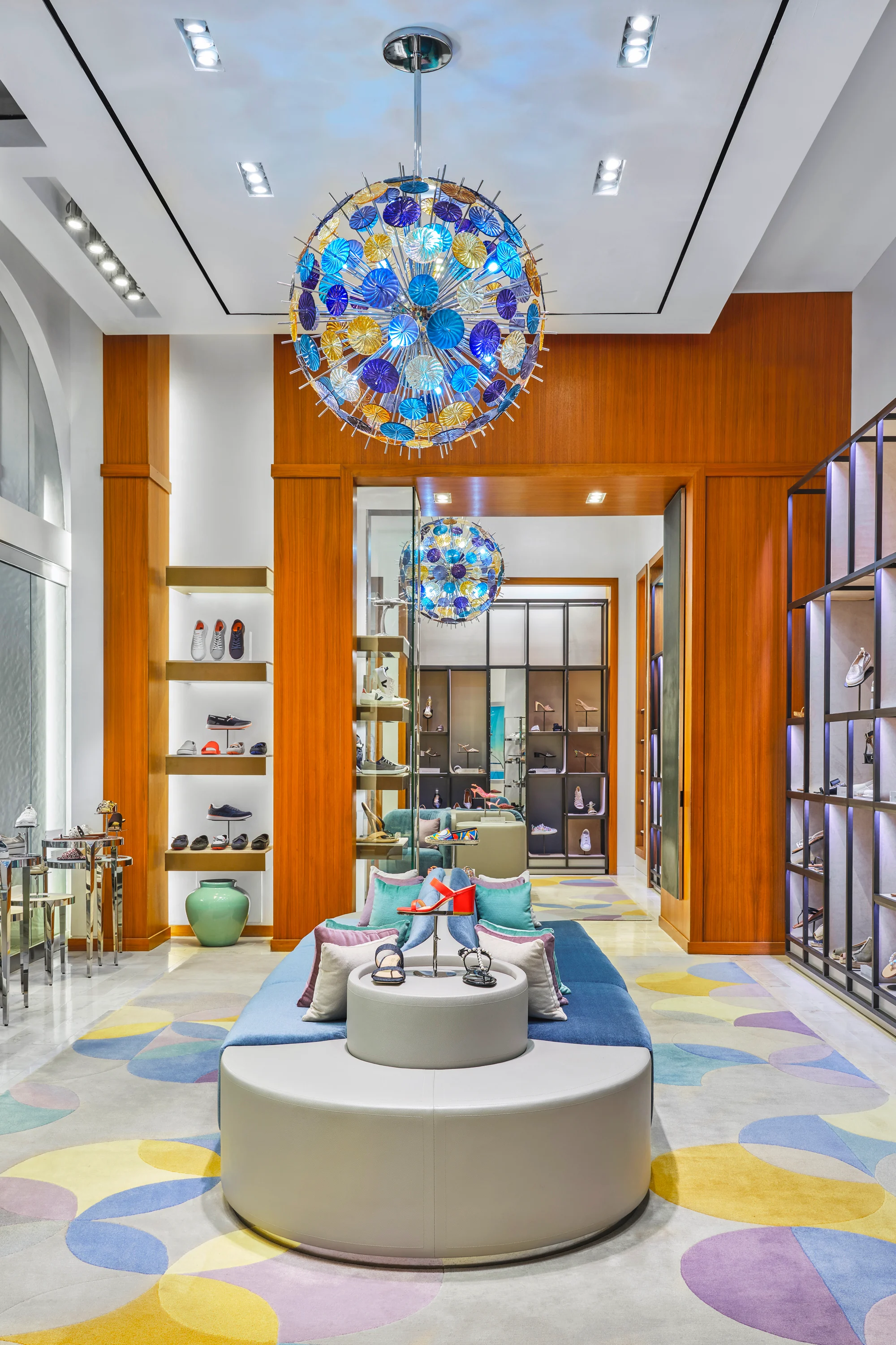 Modern retail store interior with colorful glass chandelier, wood paneling, and pastel floor design.