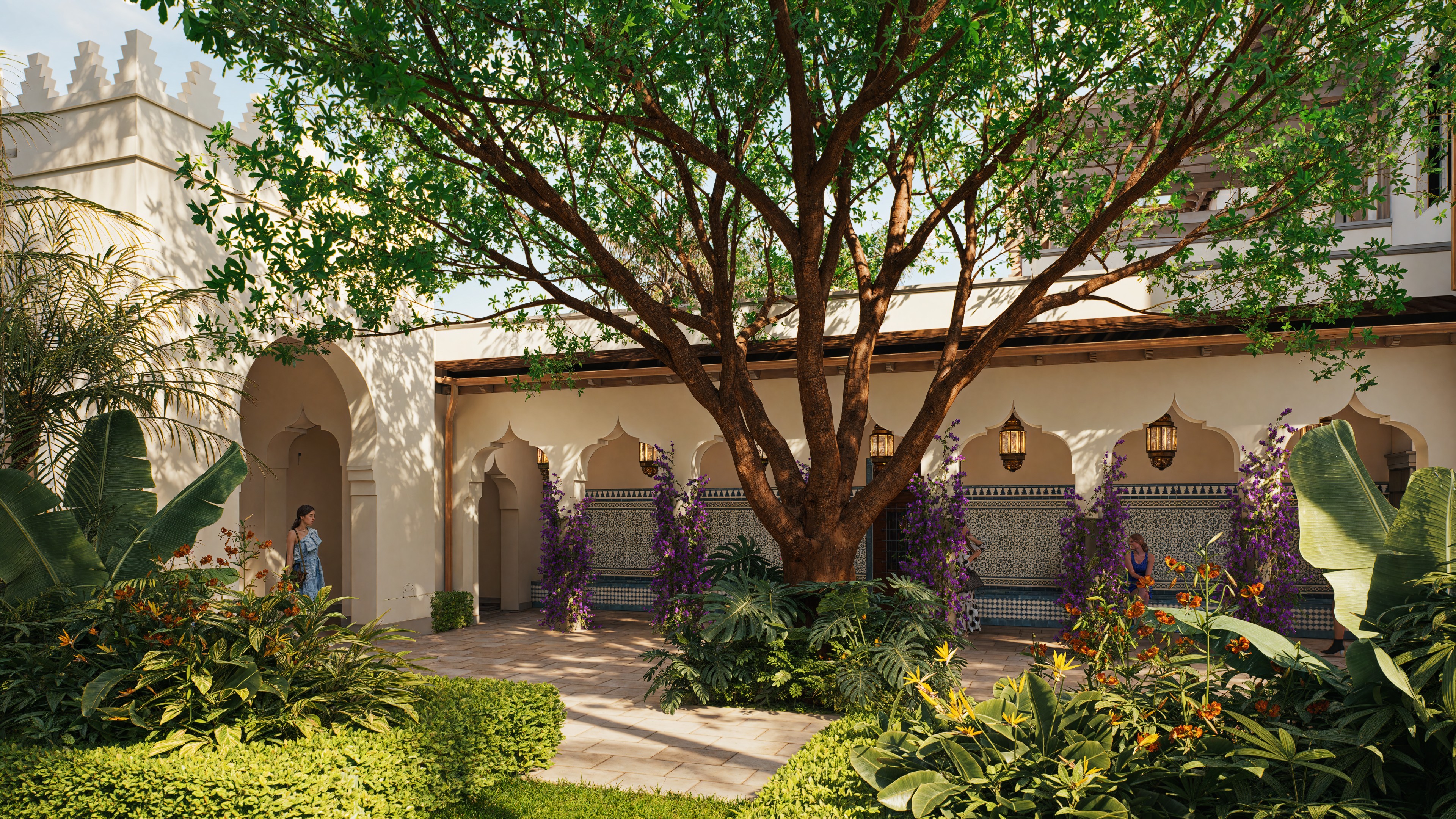 Moroccan-style courtyard with large tree, arched doorways, lanterns, and lush tropical plants.