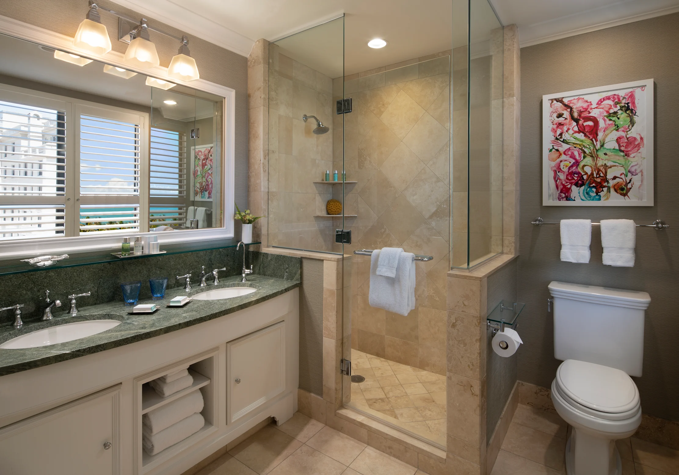 Modern bathroom with beige tile shower, white vanity with green countertop, and colorful floral art.