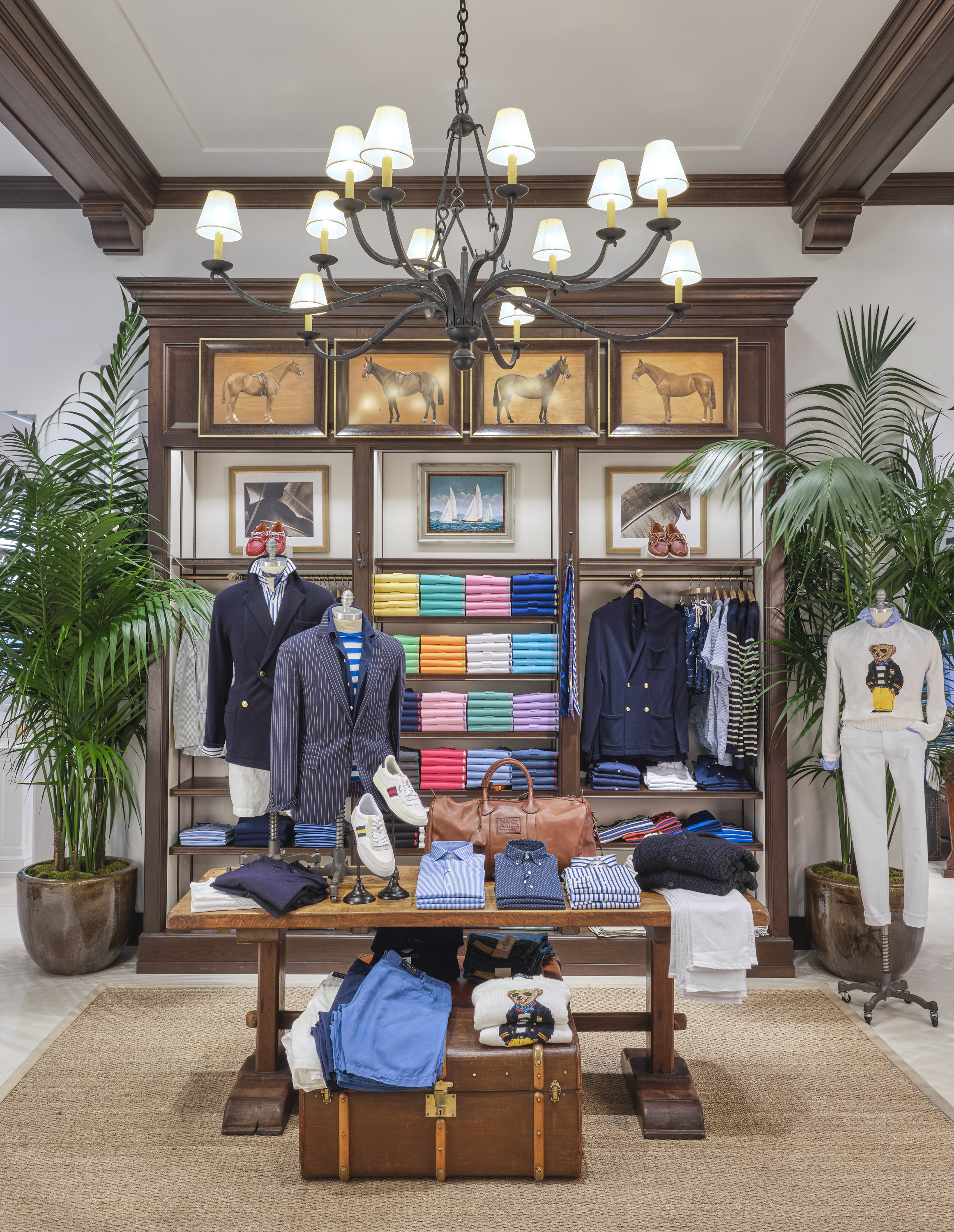 Upscale men's clothing store with dark wood fixtures, chandelier, horse paintings, and palm plants.