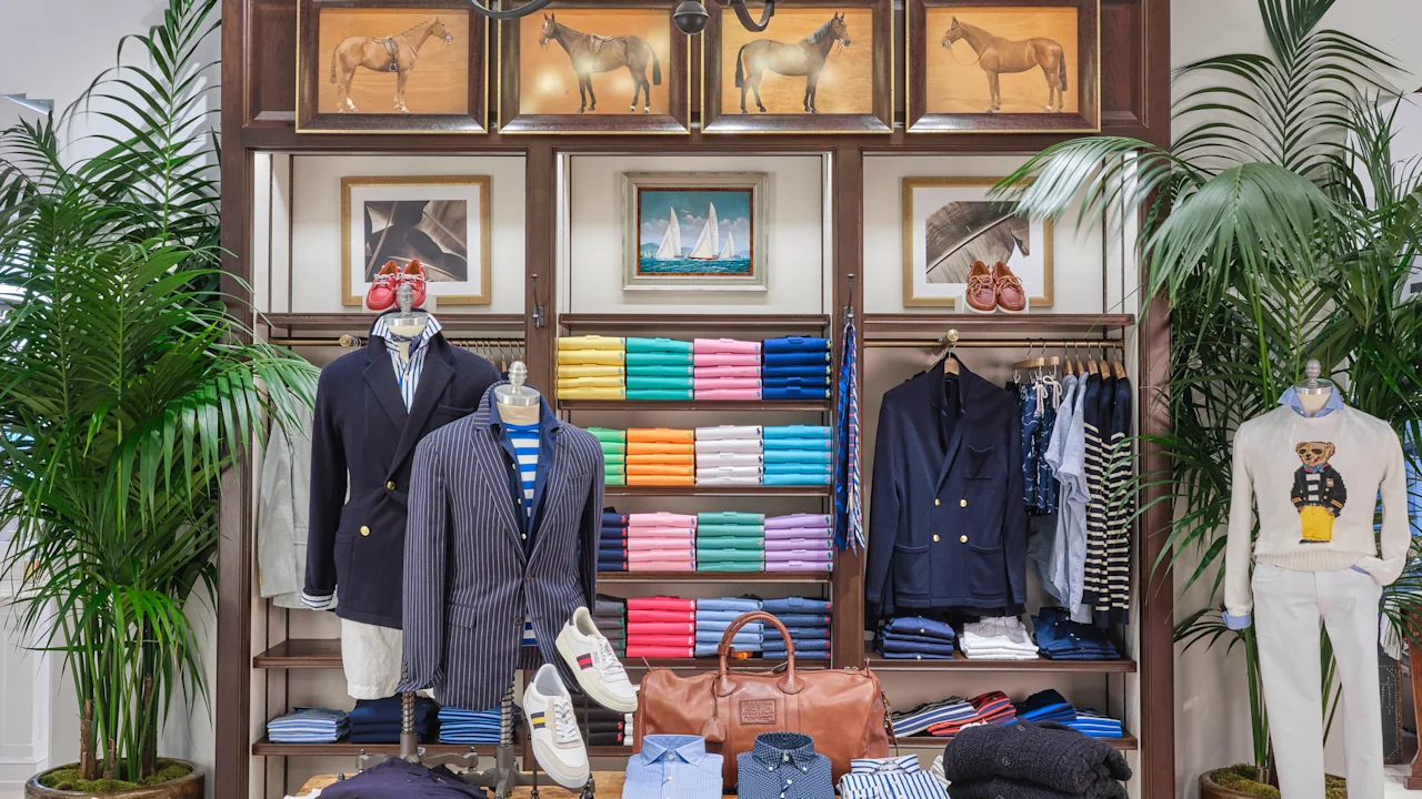Upscale men's clothing store with dark wood fixtures, chandelier, horse paintings, and palm plants.
