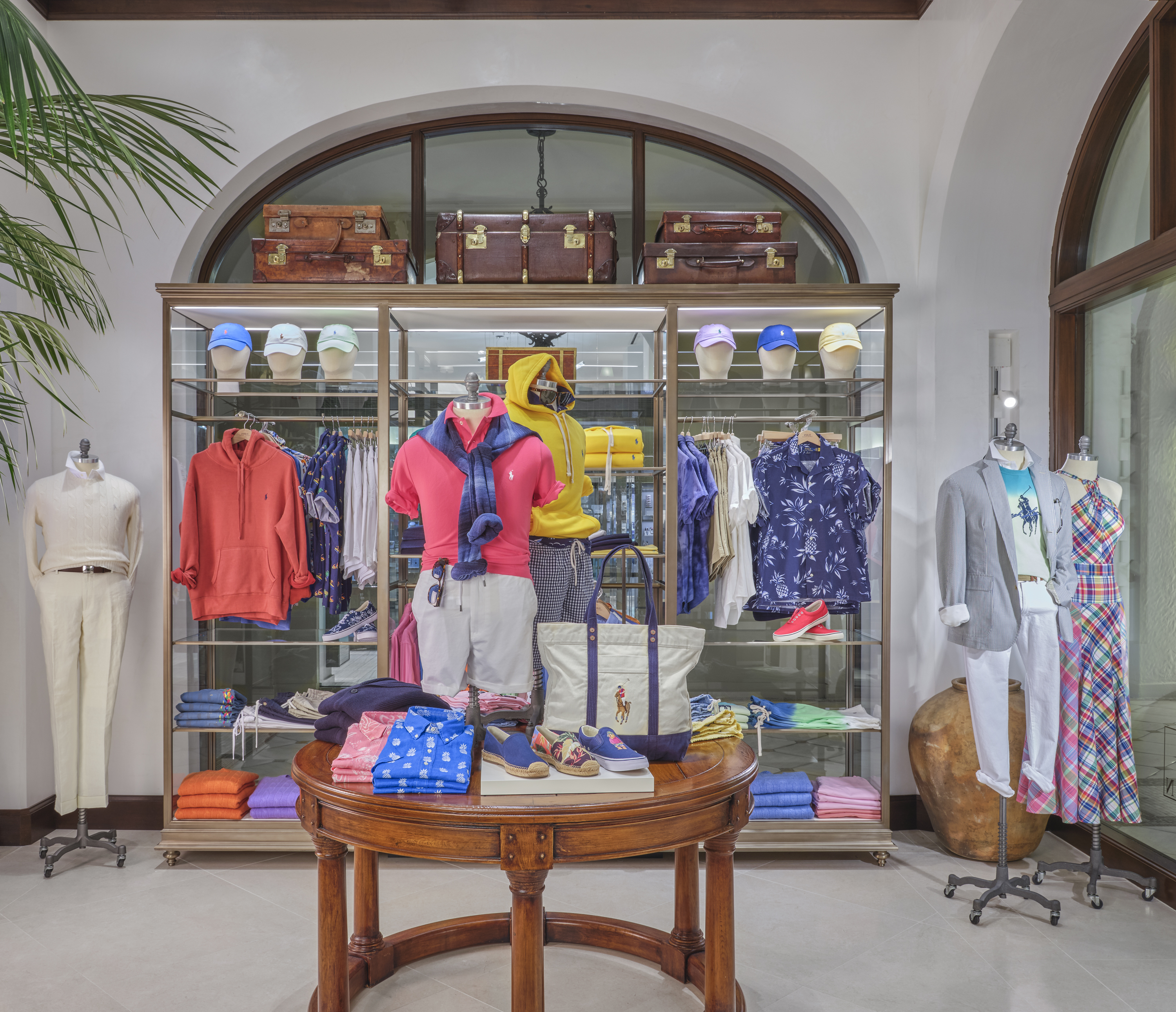 Upscale men's clothing store with dark wood fixtures, chandelier, horse paintings, and palm plants.