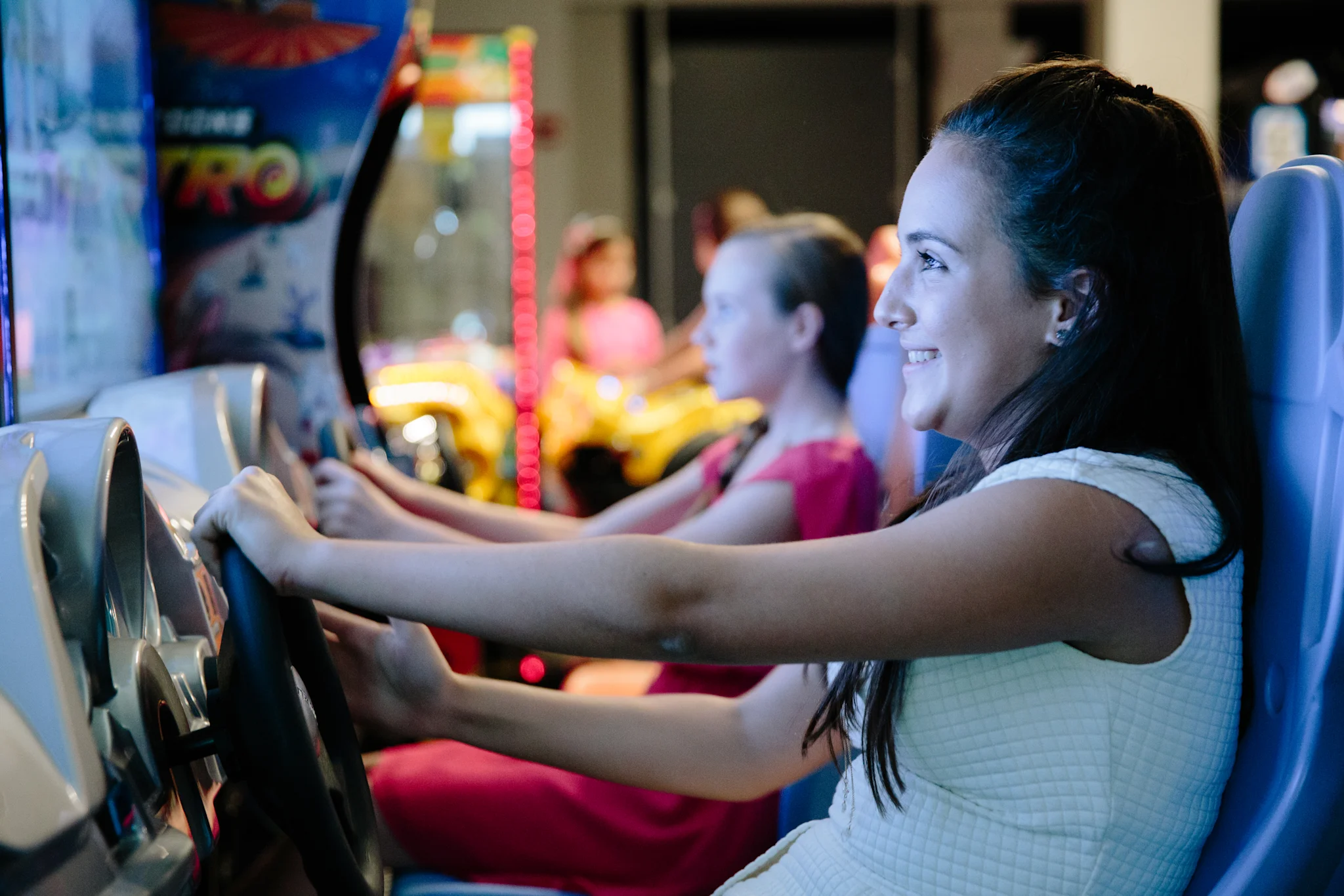 Woman smiling while playing a racing arcade game with colorful lights in the background.